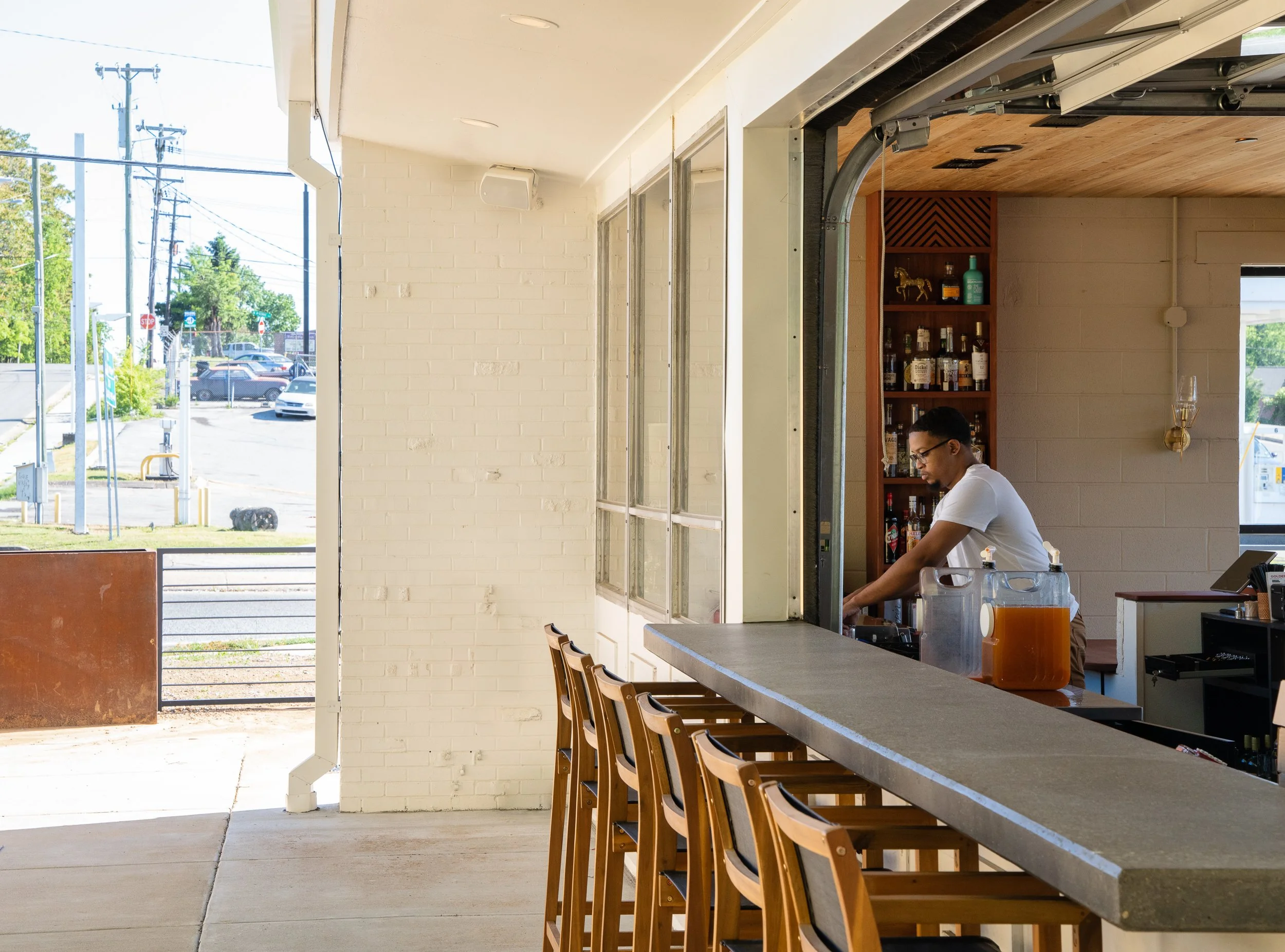 Bartender working behind an open-air bar with a retractable garage-style window.