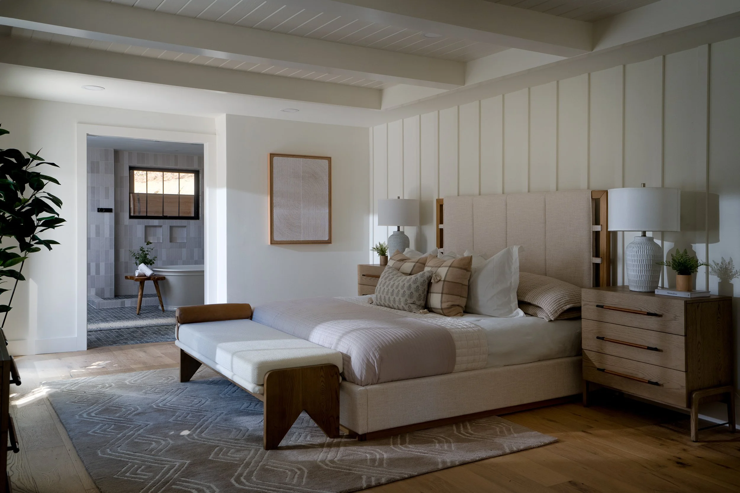 Primary bedroom with upholstered bed, paneled wall, wood nightstands, and a view into the adjoining bathroom.