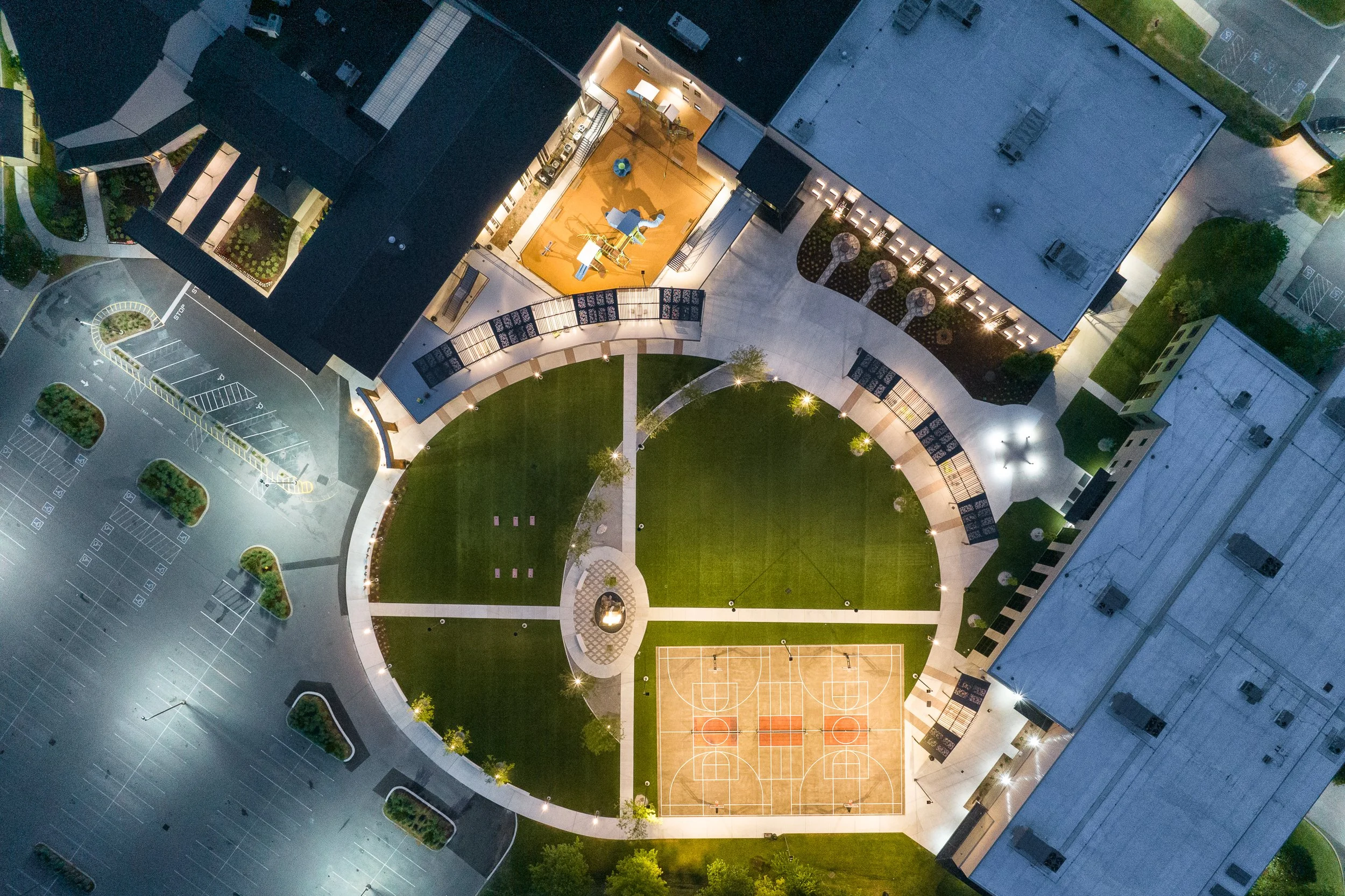 Aerial nighttime view of a modern campus with illuminated walkways and basketball court.