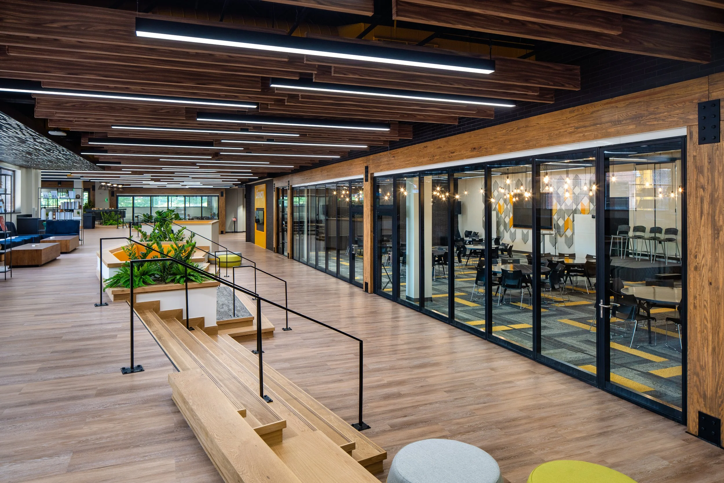 Open office space with natural wood finishes, glass partitions, and modern lighting.
