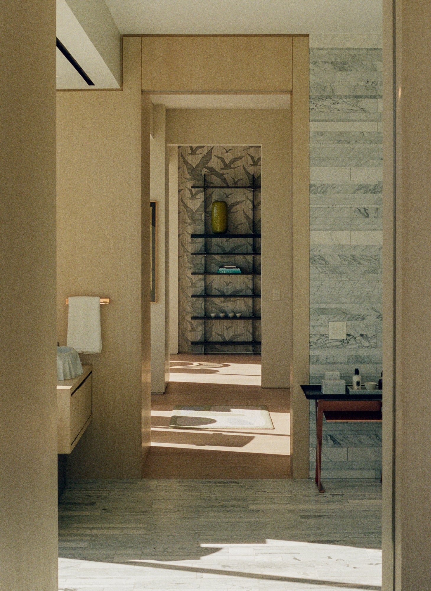 Bathroom passage framing marble tile, geometric wallcovering, custom shelving, and soft natural light.