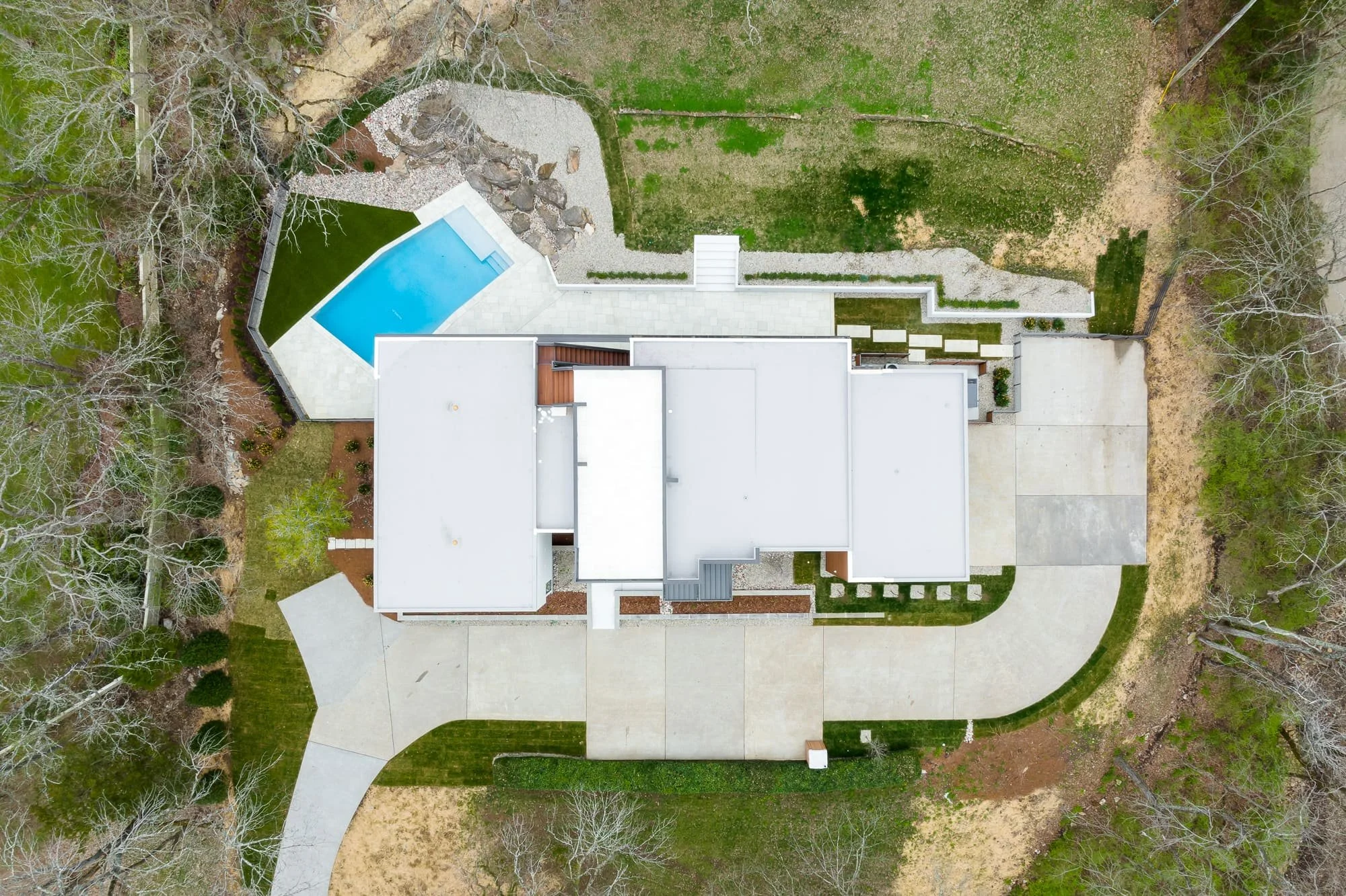 Straight-down aerial view of a modern home with a white roof, swimming pool, driveway, and landscaped yard.