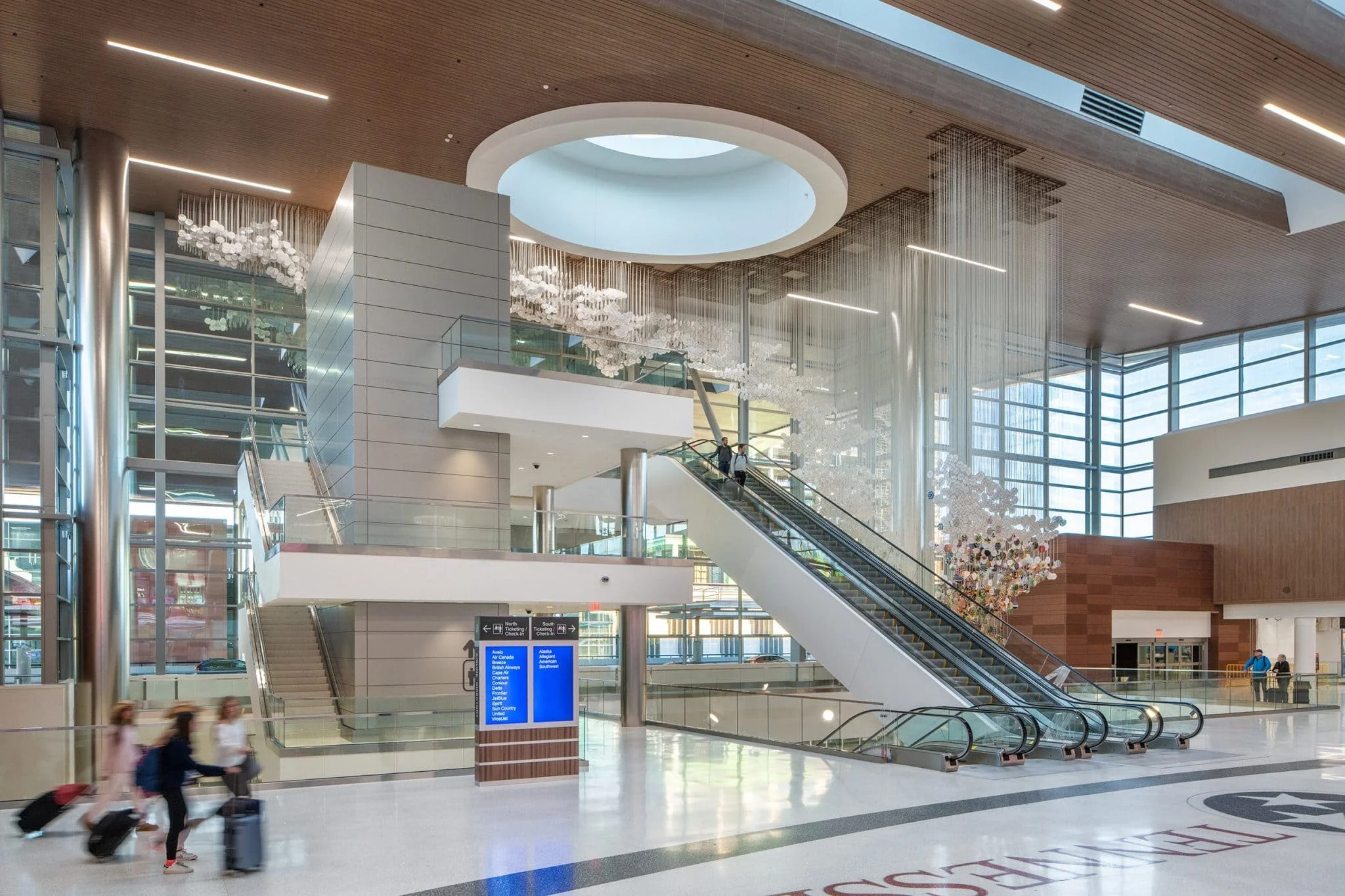 Wide view of the check-in hall with polished floors, glass railings, skylights, and artwork floating above the central space.