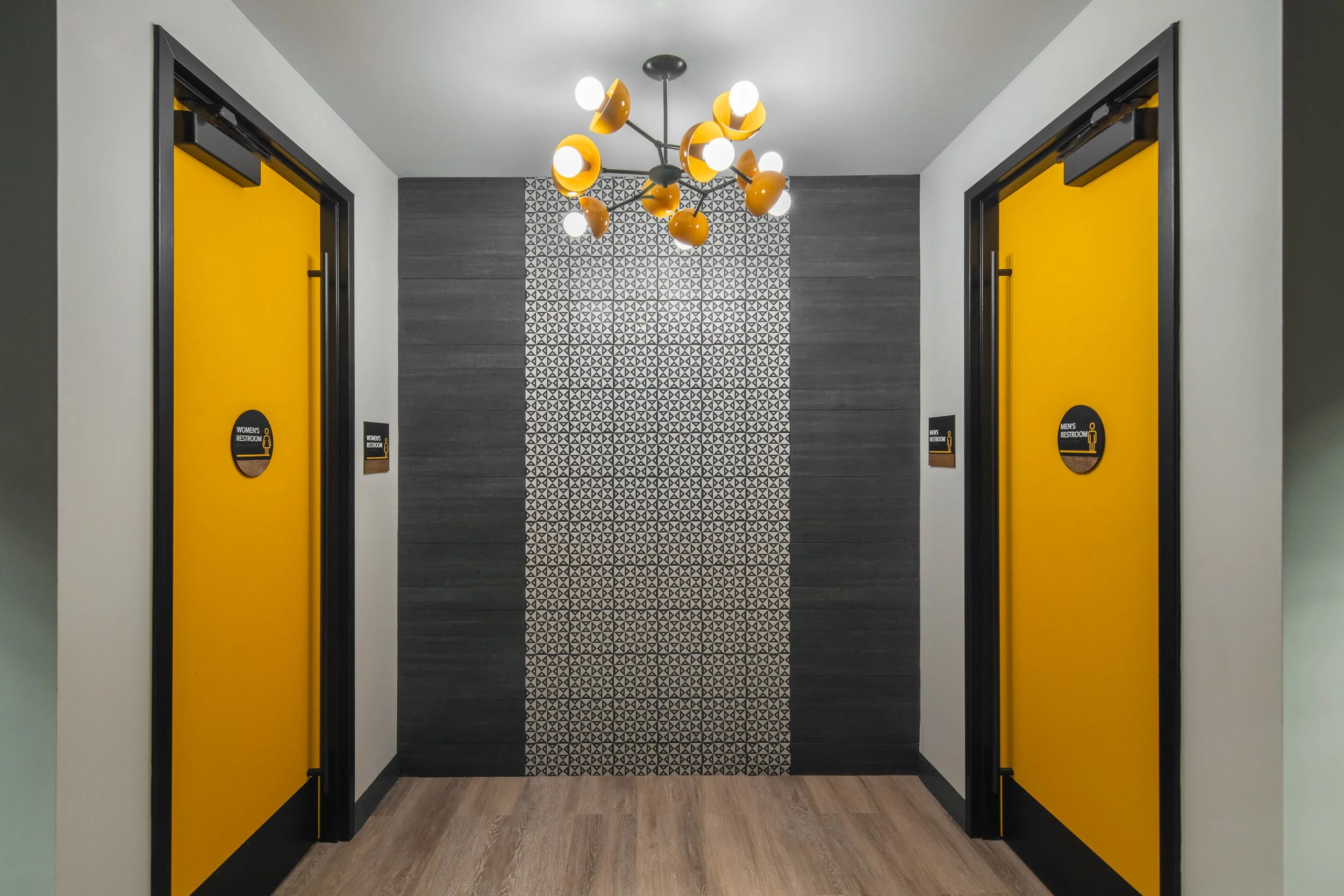 Office corridor with yellow restroom doors and a modern chandelier.