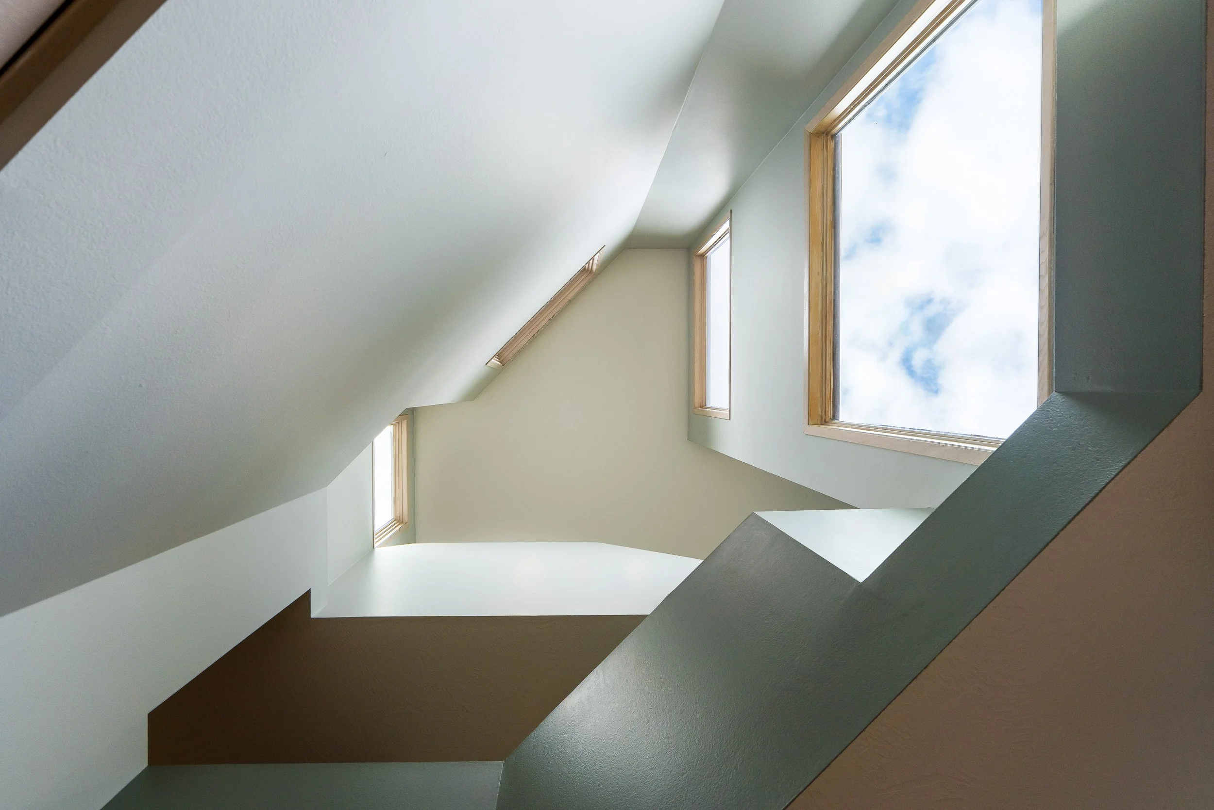 Modern staircase with angular walls and large windows bringing in daylight.