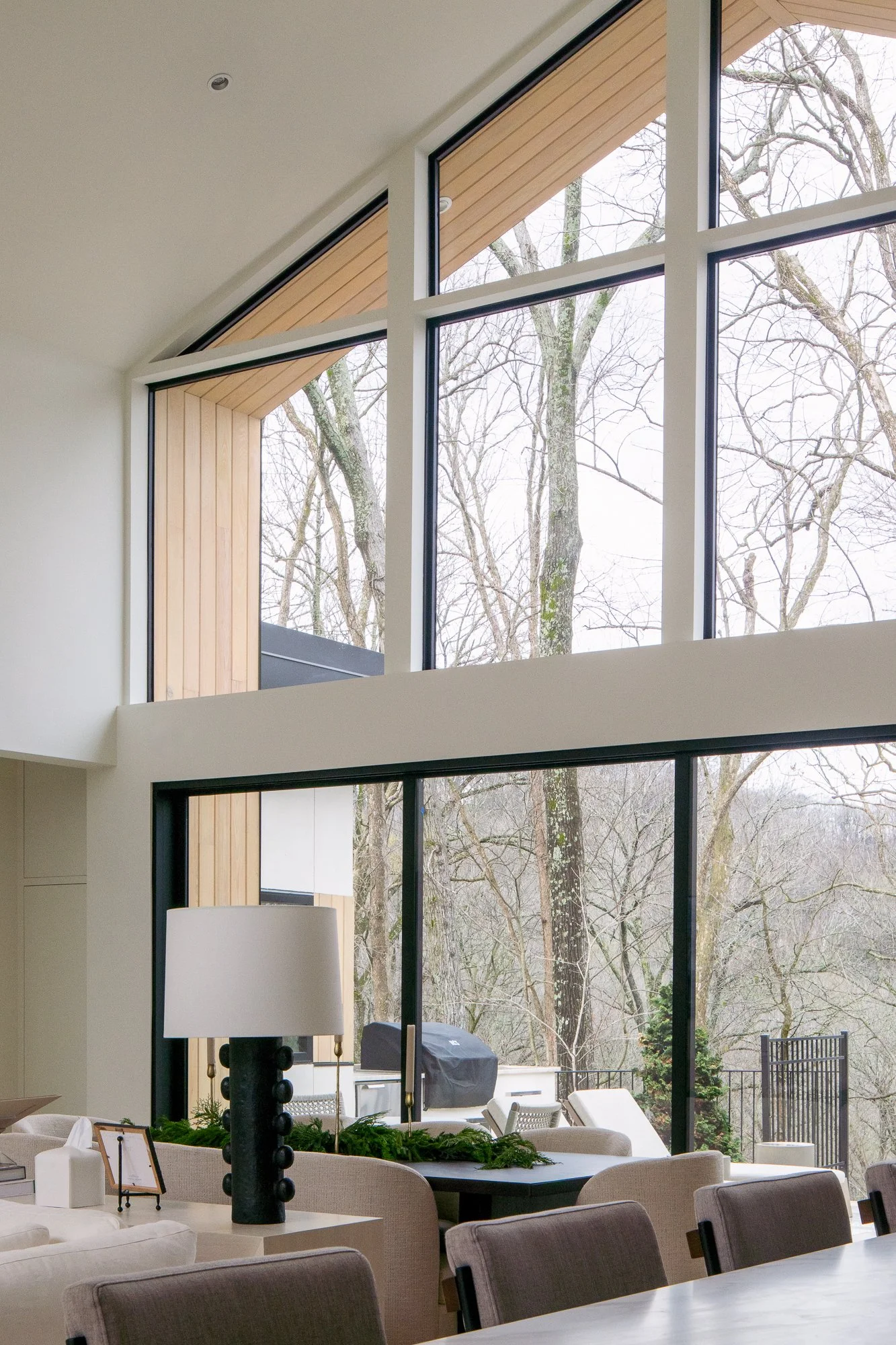 Black-framed gabled windows and tall glazing overlooking a wooded hillside.