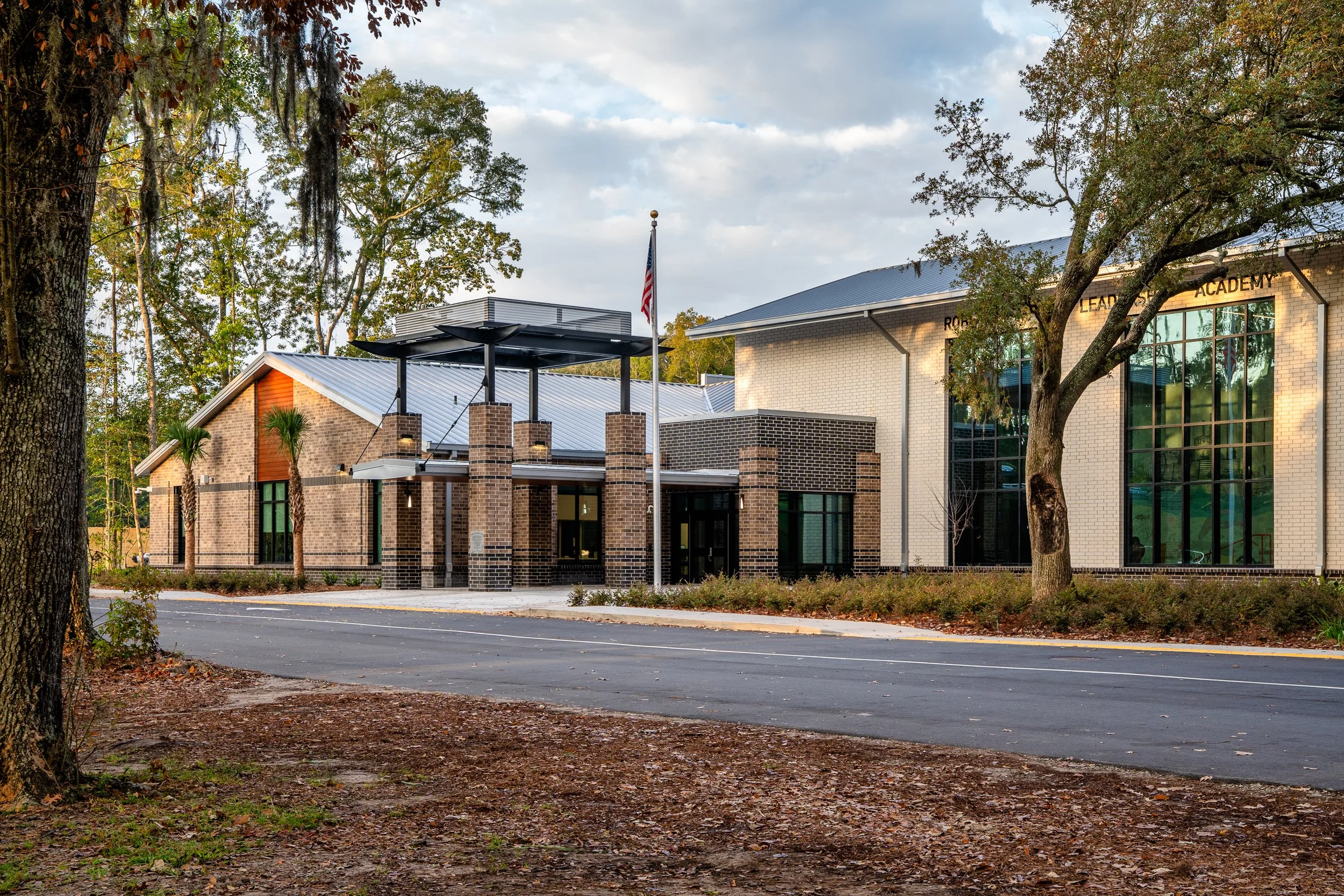 Main entry approach to Robert Smalls Leadership Academy with brick columns, metal canopy, flagpole, and live oaks around the campus.