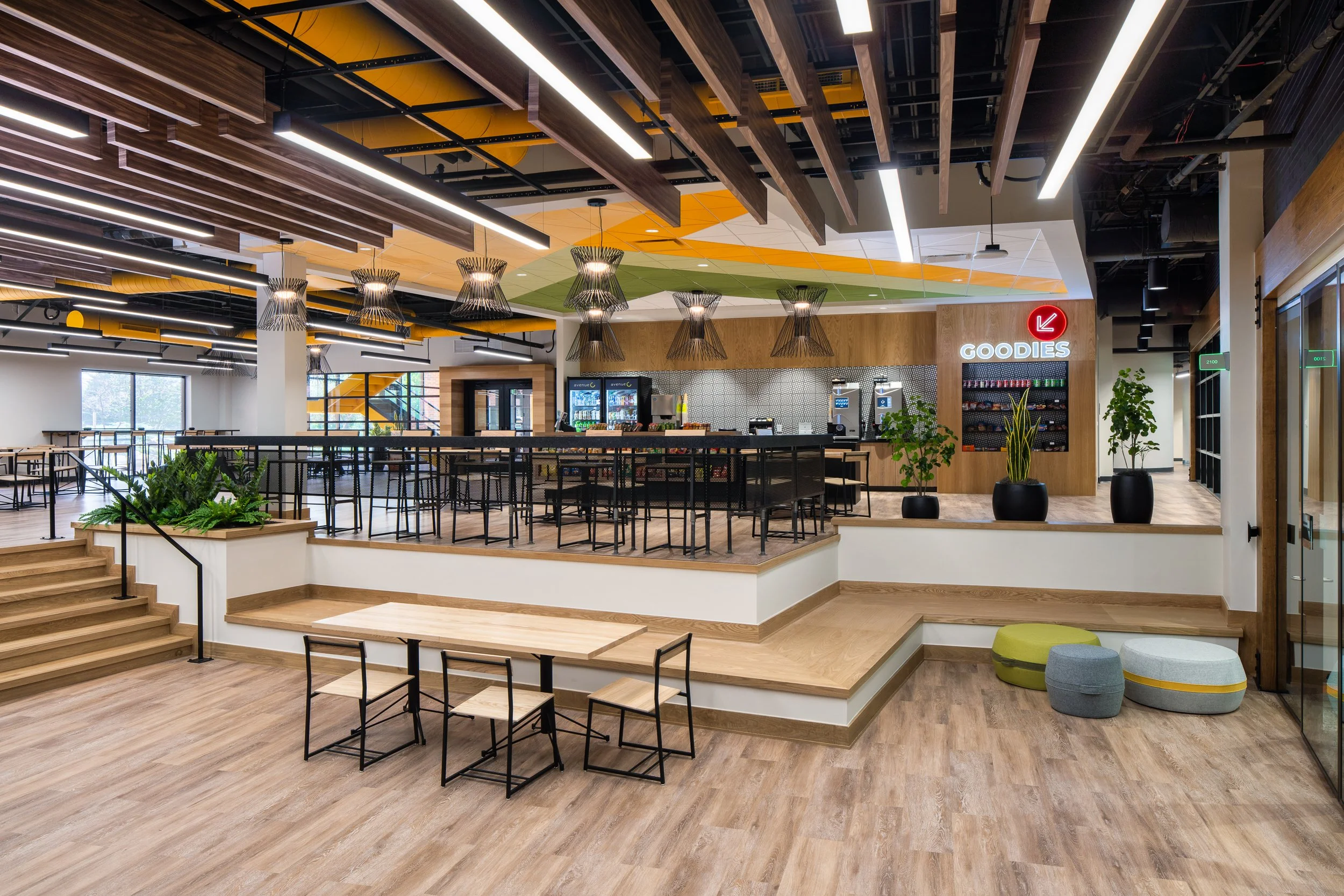 Spacious corporate cafeteria with wood finishes, bold color accents, and modern lighting.