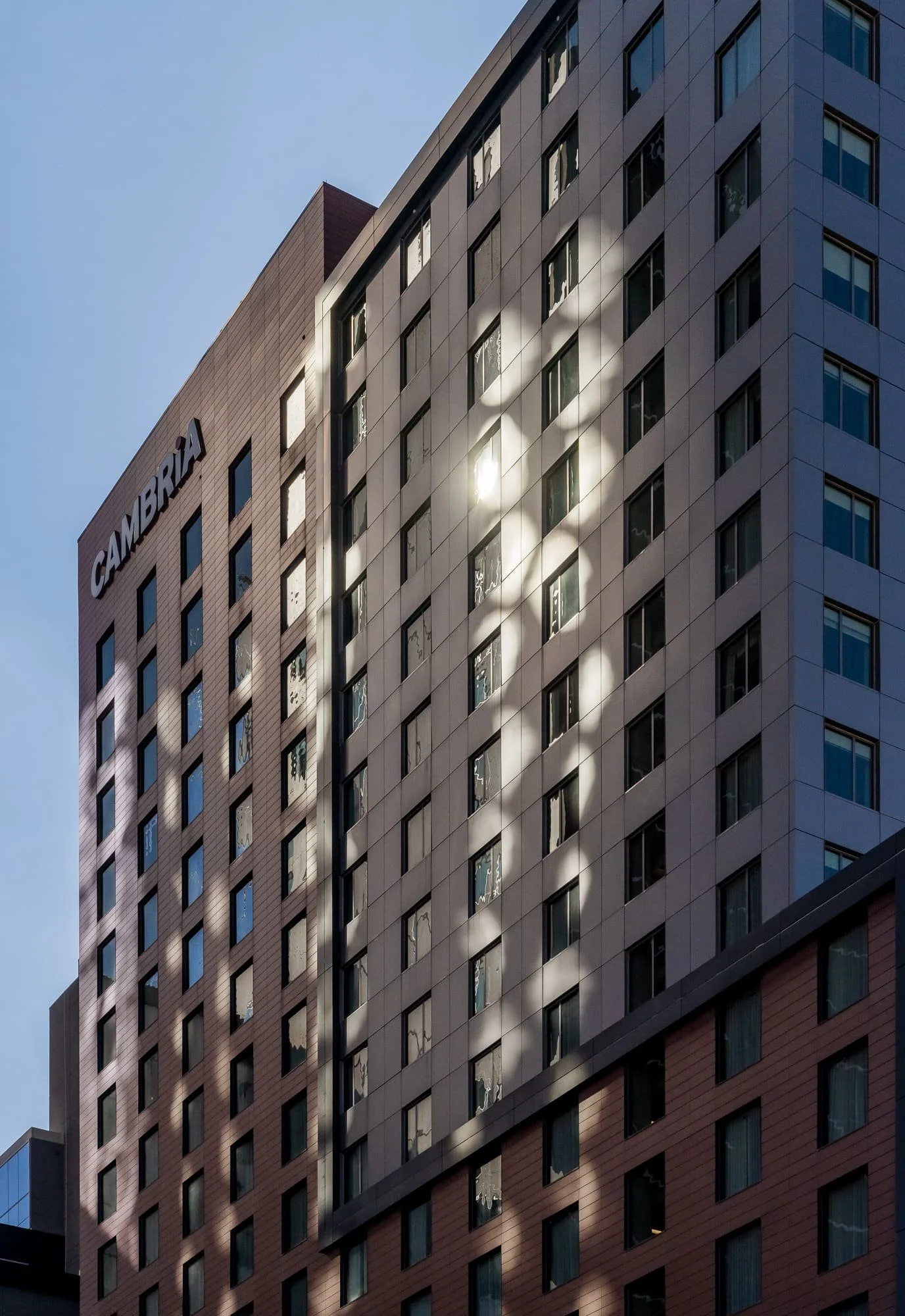 Detail of the Cambria Hotel rear facade in afternoon with bright reflected sunlight patterns scattered across the dark cladding from neighboring buildings