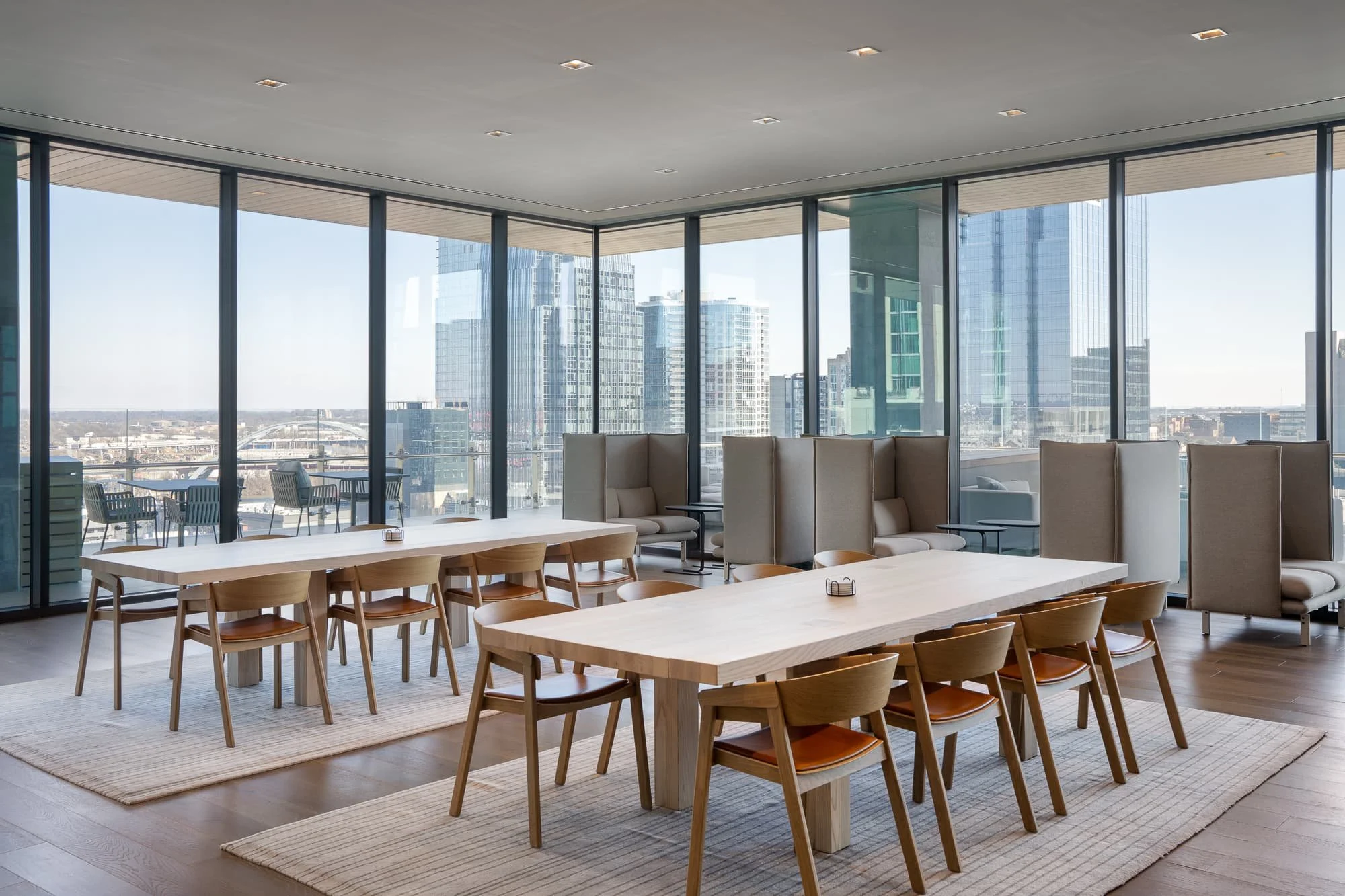 Corner dining and lounge area at Alliance Bernstein Nashville with floor-to-ceiling glass on two sides, wood tables, leather chairs, and panoramic views of the downtown skyline