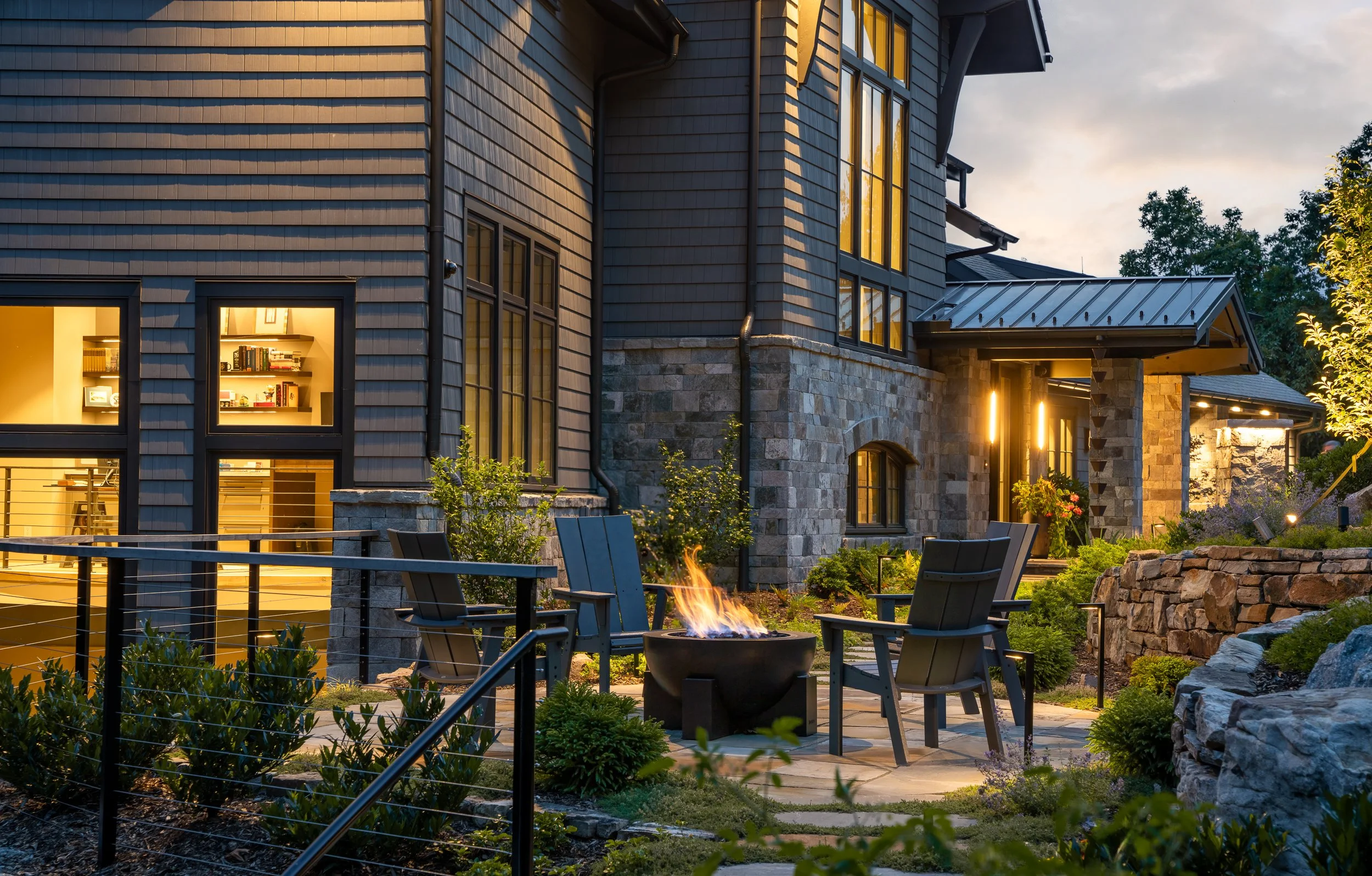 Outdoor seating area with firepit, modern chairs, and illuminated exterior.