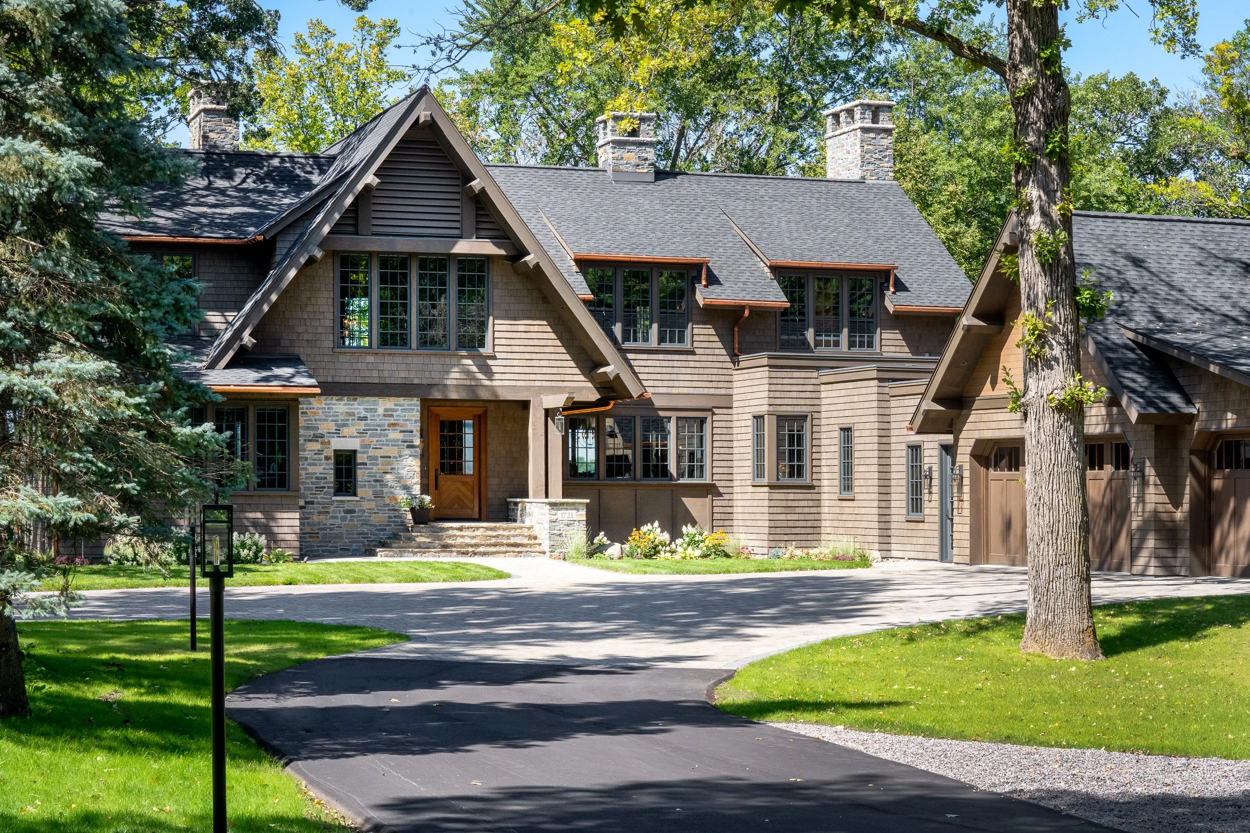 Craftsman-style home with stone and cedar exterior near wooded drive.