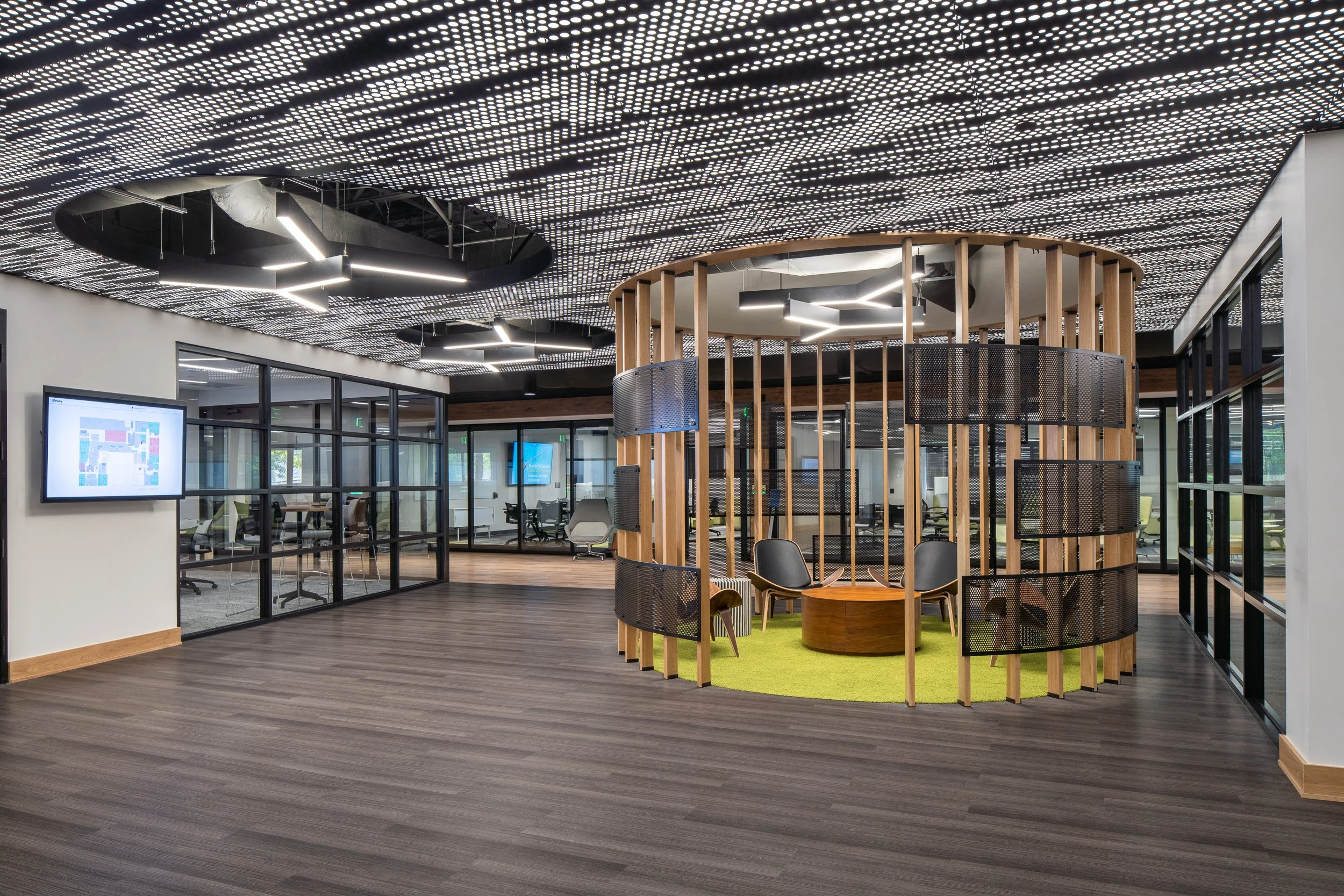 Open workspace with a circular wooden meeting pod and perforated ceiling panels.