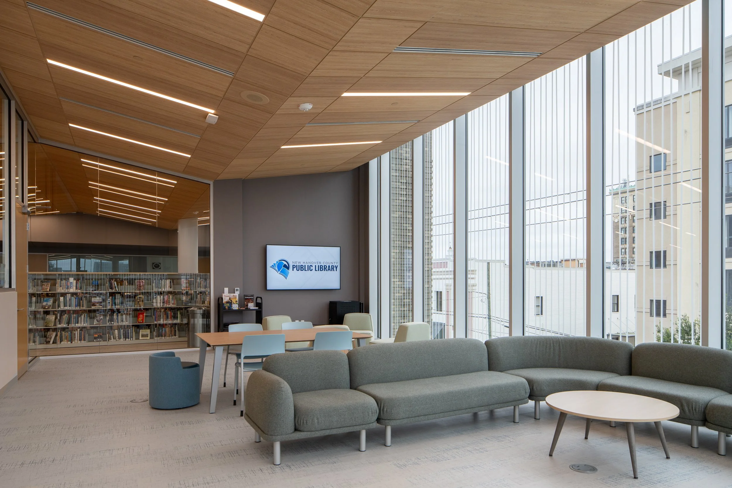 Quiet lounge area with large windows, soft seating, study tables, and New Hanover County Public Library signage.