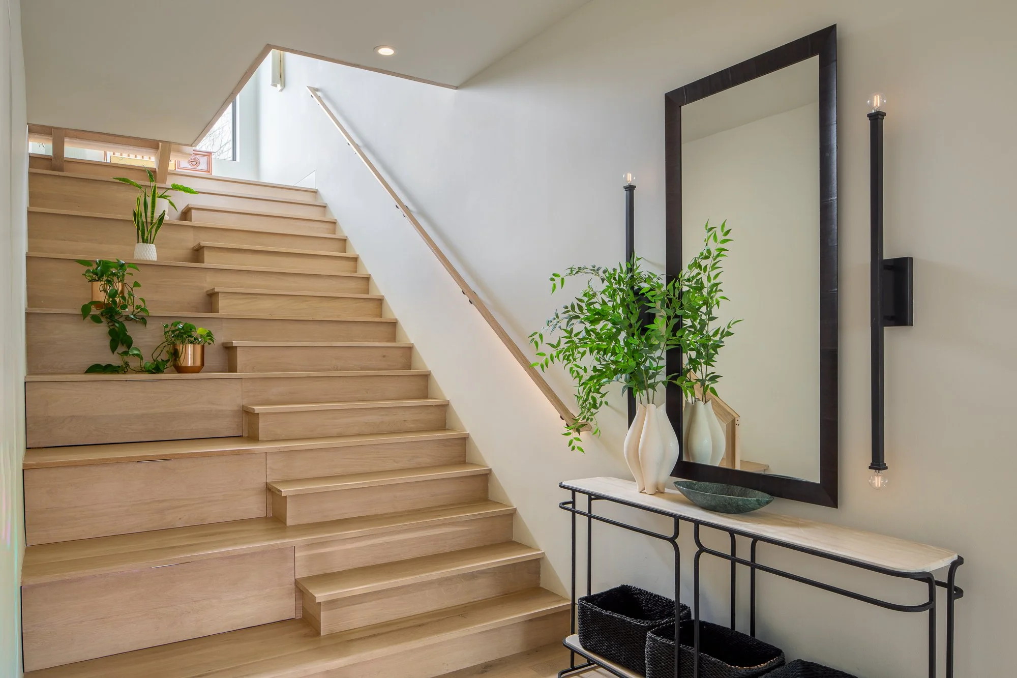 Modern staircase with built-in storage steps, console table, and oversized mirror.