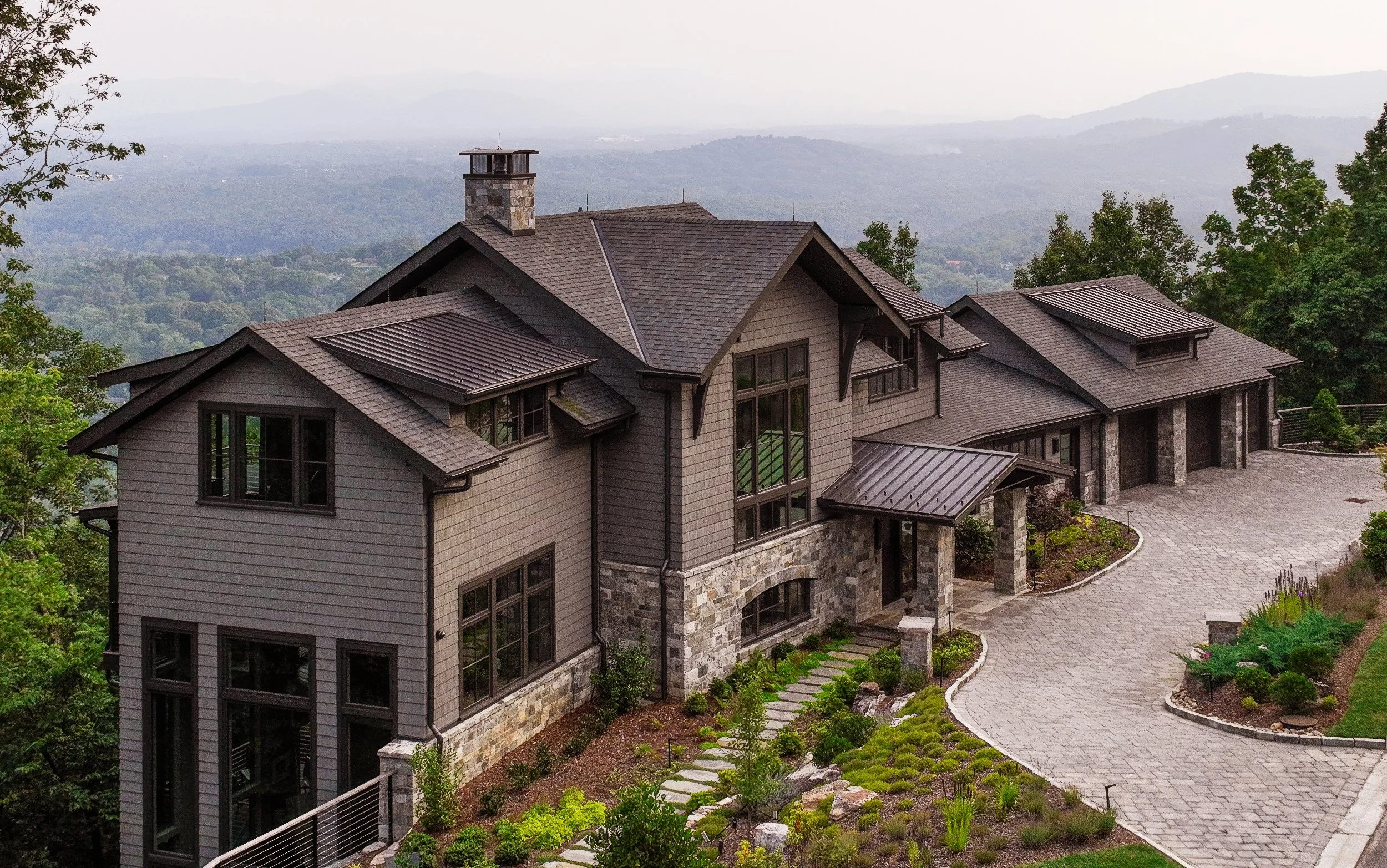 Mountain home exterior with stone walls, wood siding, landscaped entry, and distant Blue Ridge views.
