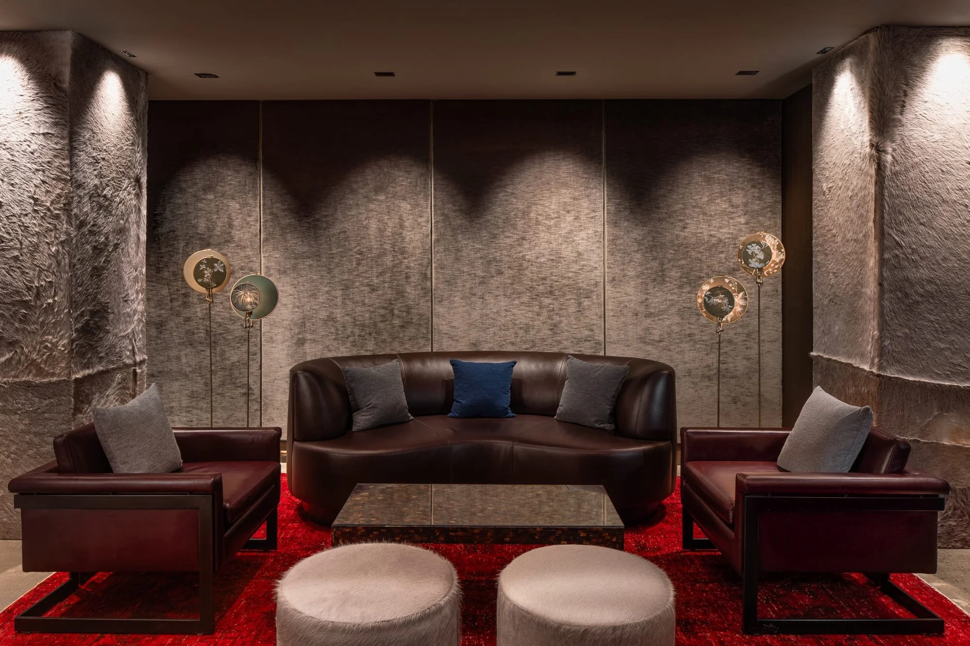 Symmetrical lounge seating with a brown leather sofa, red rug, textured wall panels, and warm accent lighting in a luxury hospitality interior.