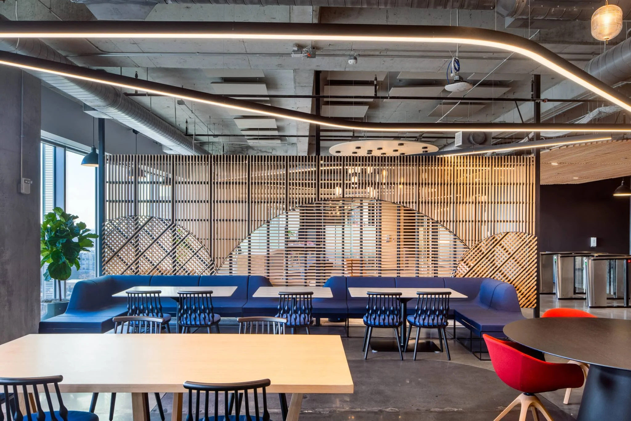 Dining area with blue banquette seating, wood privacy screens, black chairs, and exposed ceiling lights.