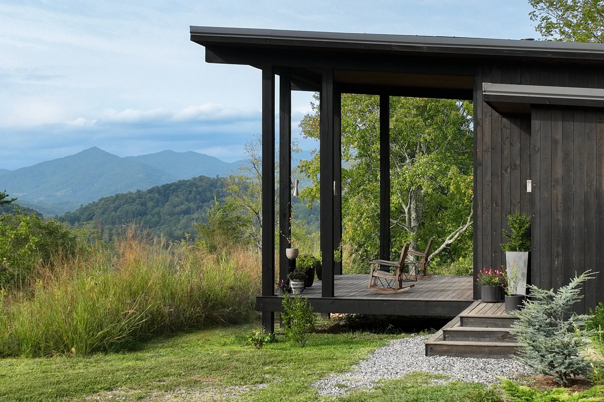 Modern mountain porch with dark siding, outdoor seating, and layered Blue Ridge views.