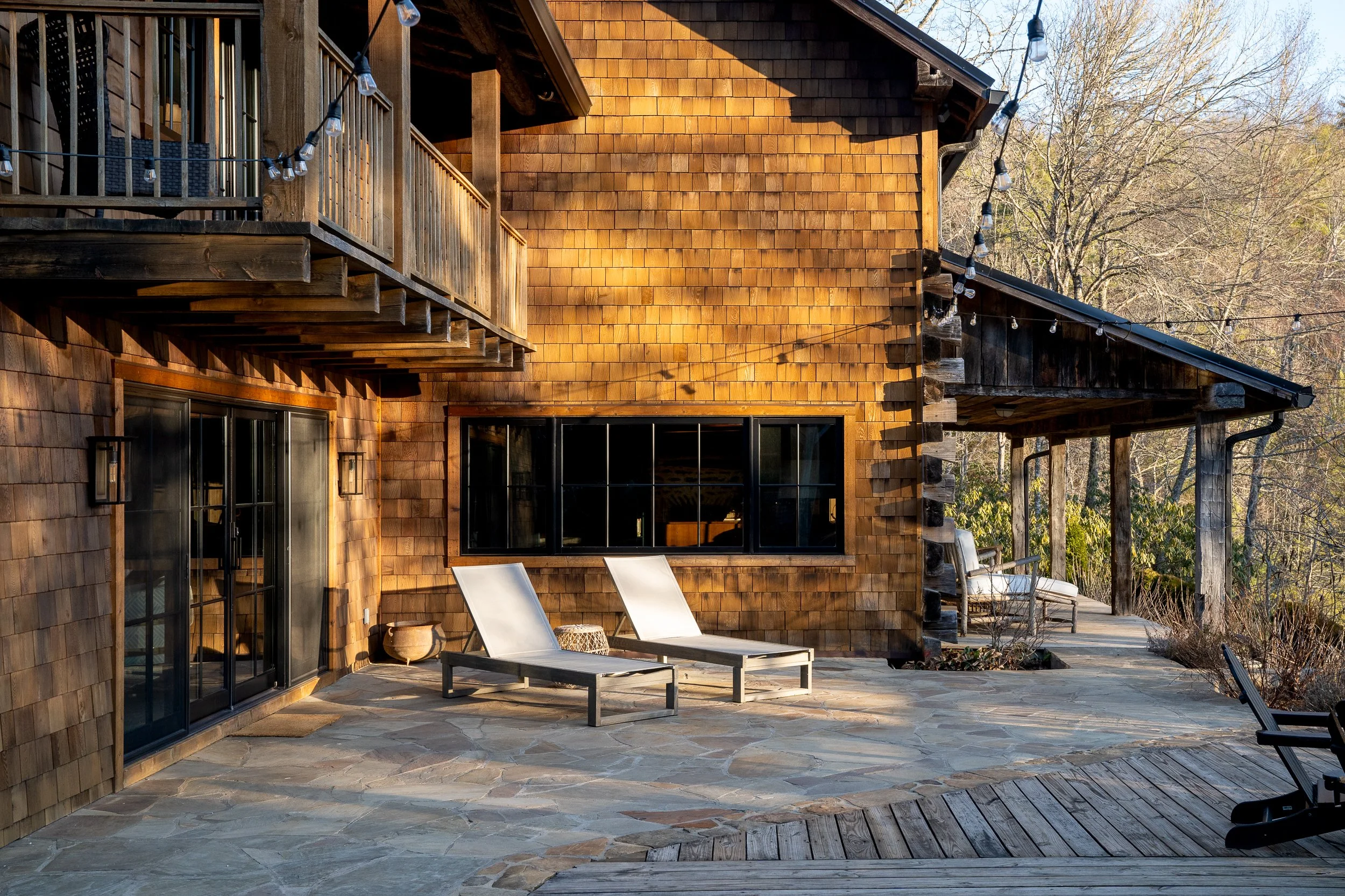 Wood-shingle mountain home patio with lounge chairs, stone paving, and warm afternoon light.