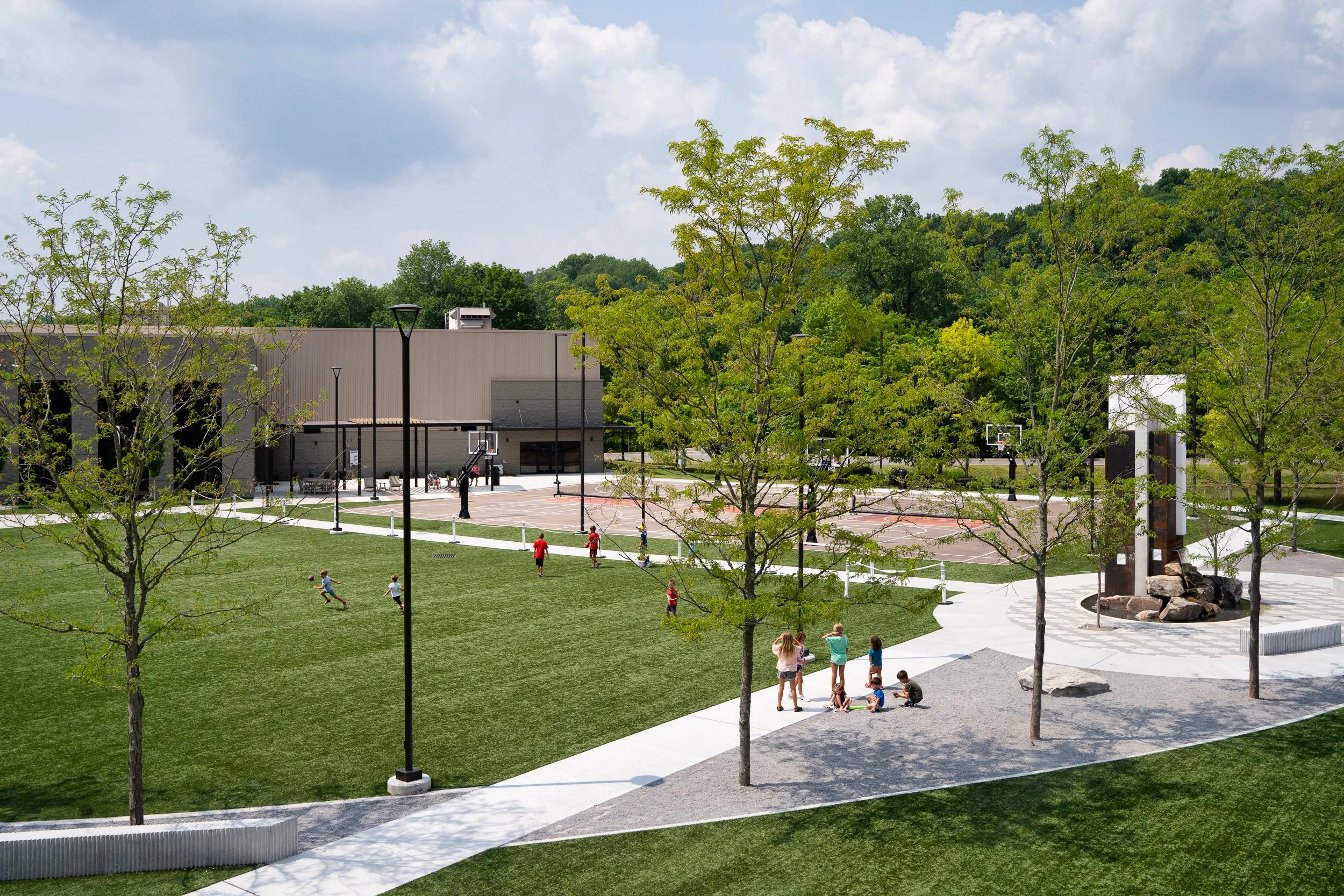 Green space with walking paths, trees, and a recreational area with kids playing.