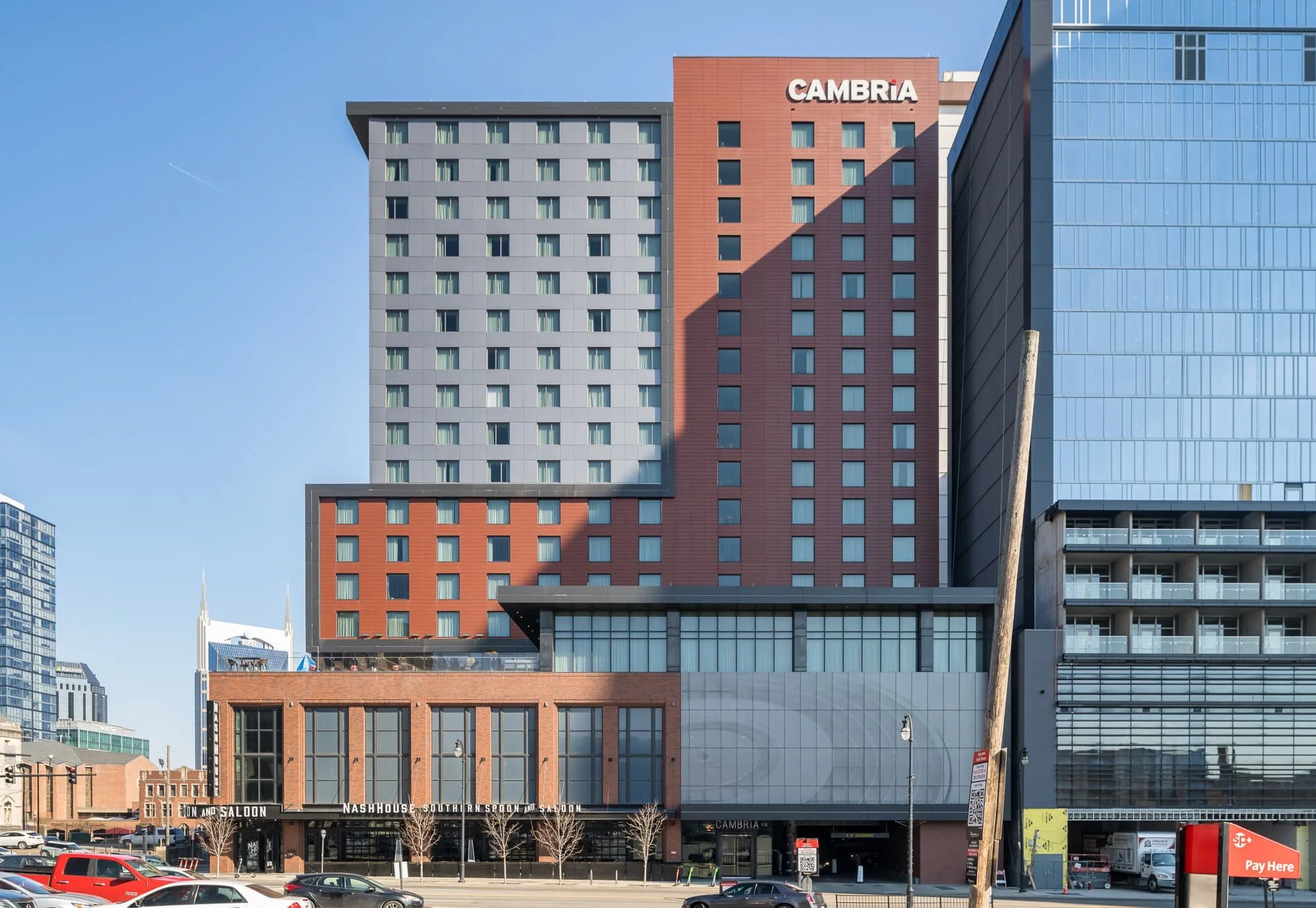 Cambria Hotel in downtown Nashville at noon with a harsh diagonal shadow cast across the red and gray facade from the adjacent 1 Hotel under construction