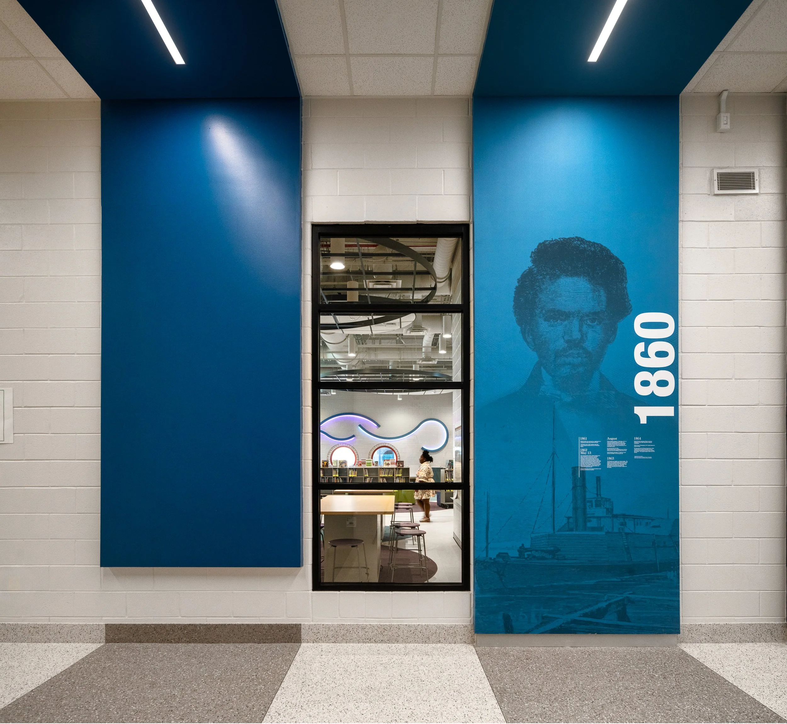 Blue wall graphic with large 1860 typography and portrait artwork beside an interior classroom window at the academy.