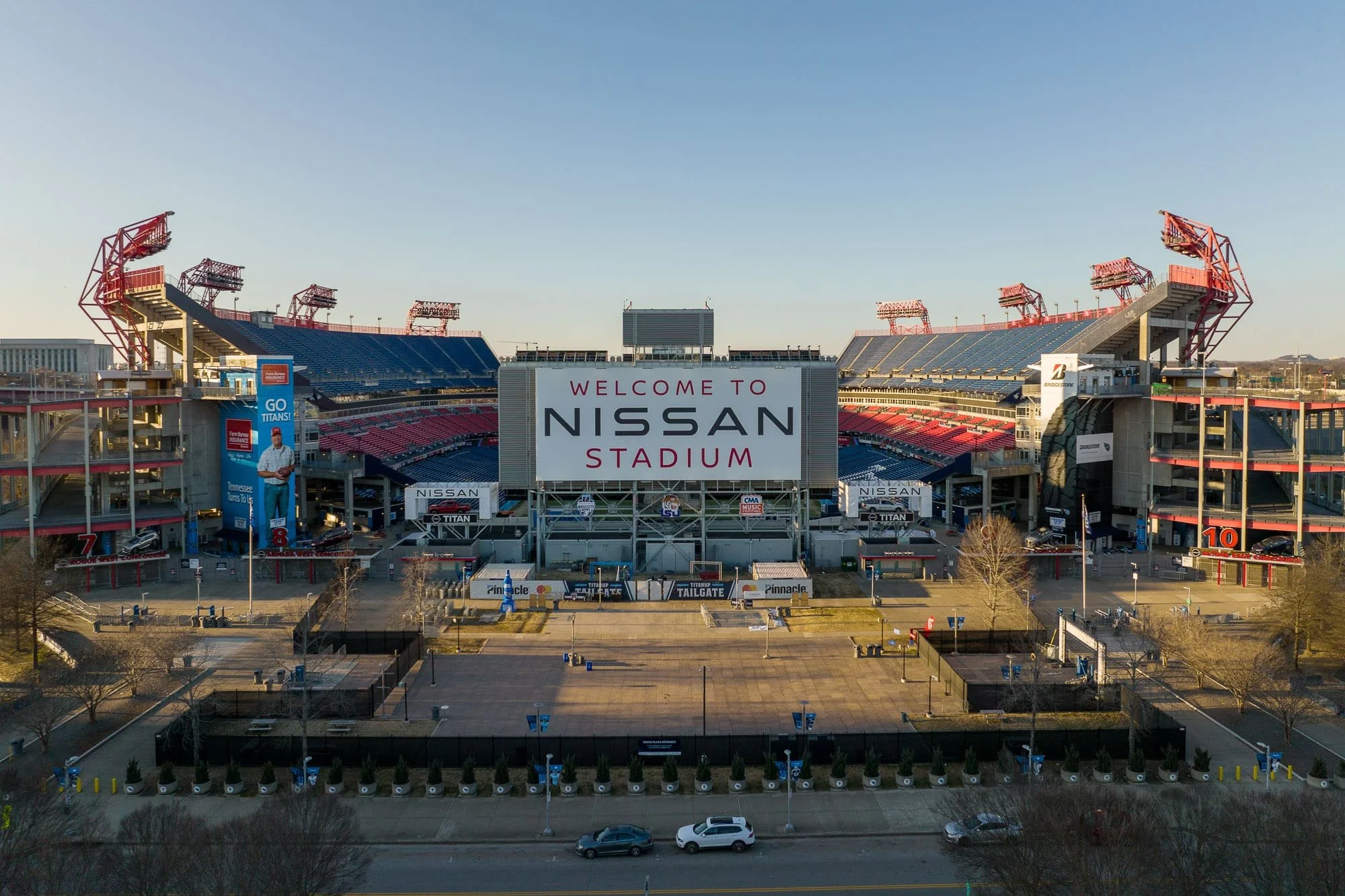 Aerial drone view of Nissan Stadium in Nashville from the front showing the Welcome to Nissan Stadium signage, red light towers, and surrounding parking and roads