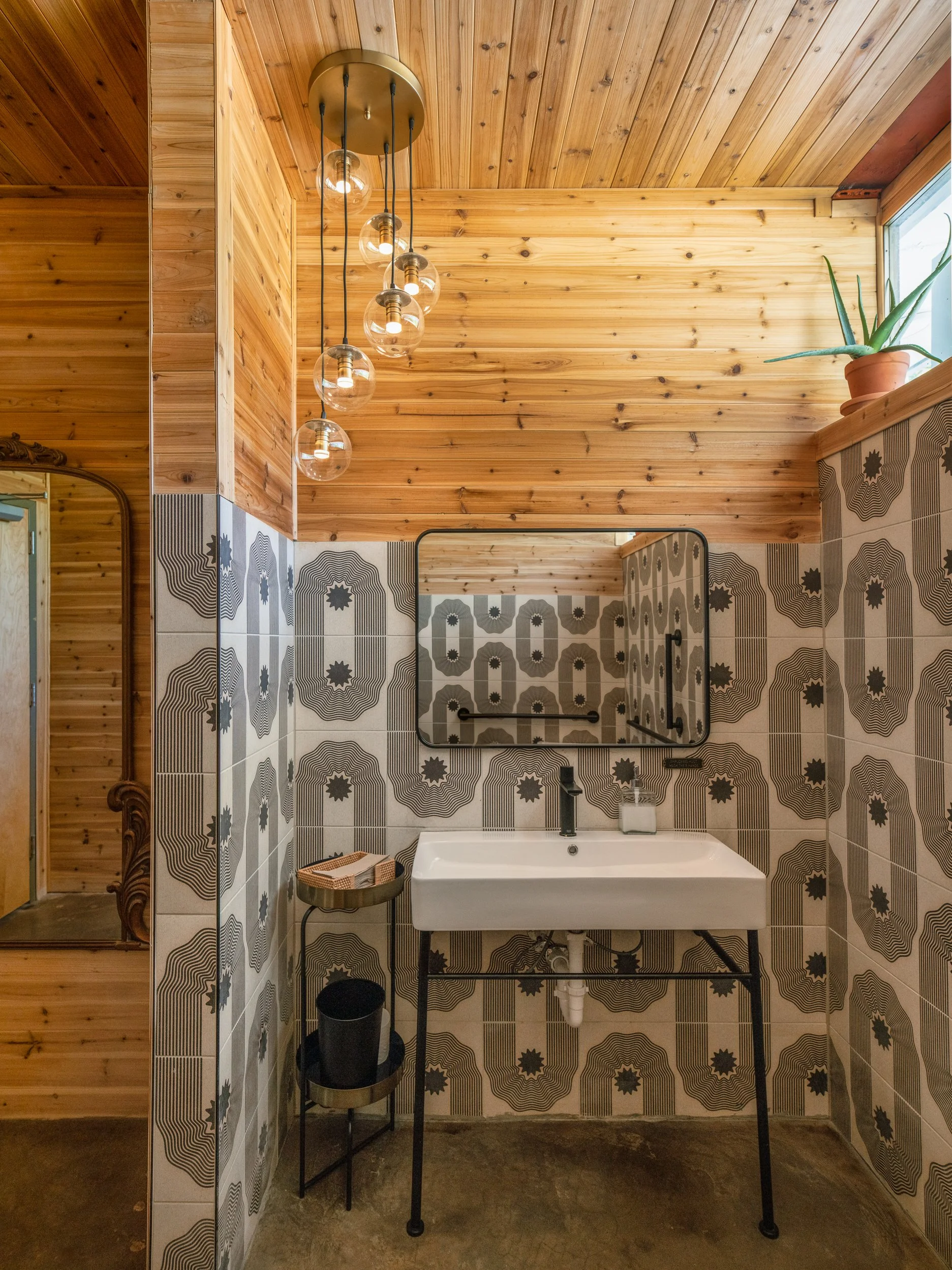 Bathroom with geometric tile walls, wood-paneled ceiling, and globe pendant lighting.