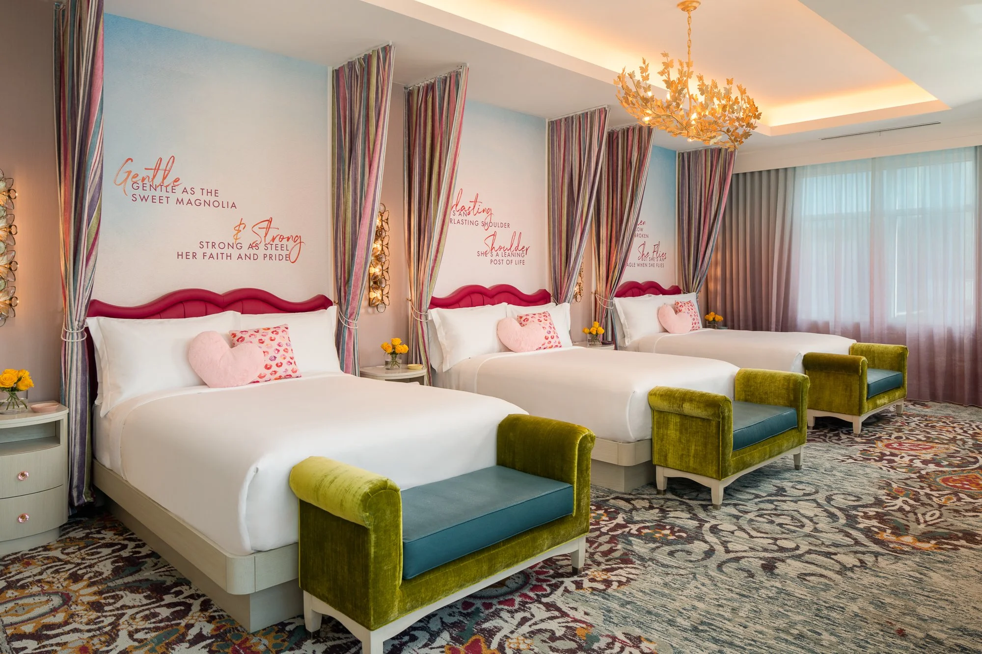 Three-bed SongTeller Hotel suite with striped canopy drapery, pink headboards, green benches, colorful carpet, and custom wall lettering.