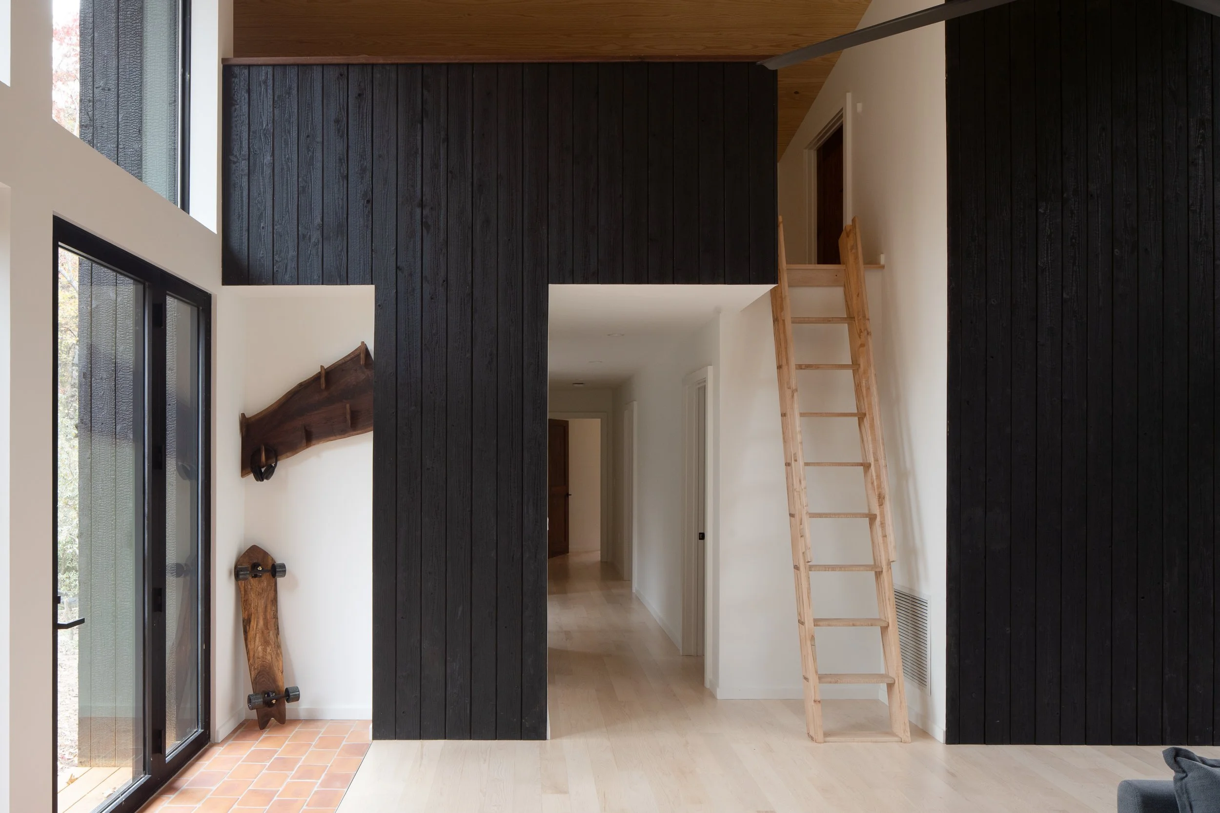 Interior view with burnt cedar walls, pale floors, a wood ladder, and sliding glass doors to the deck.