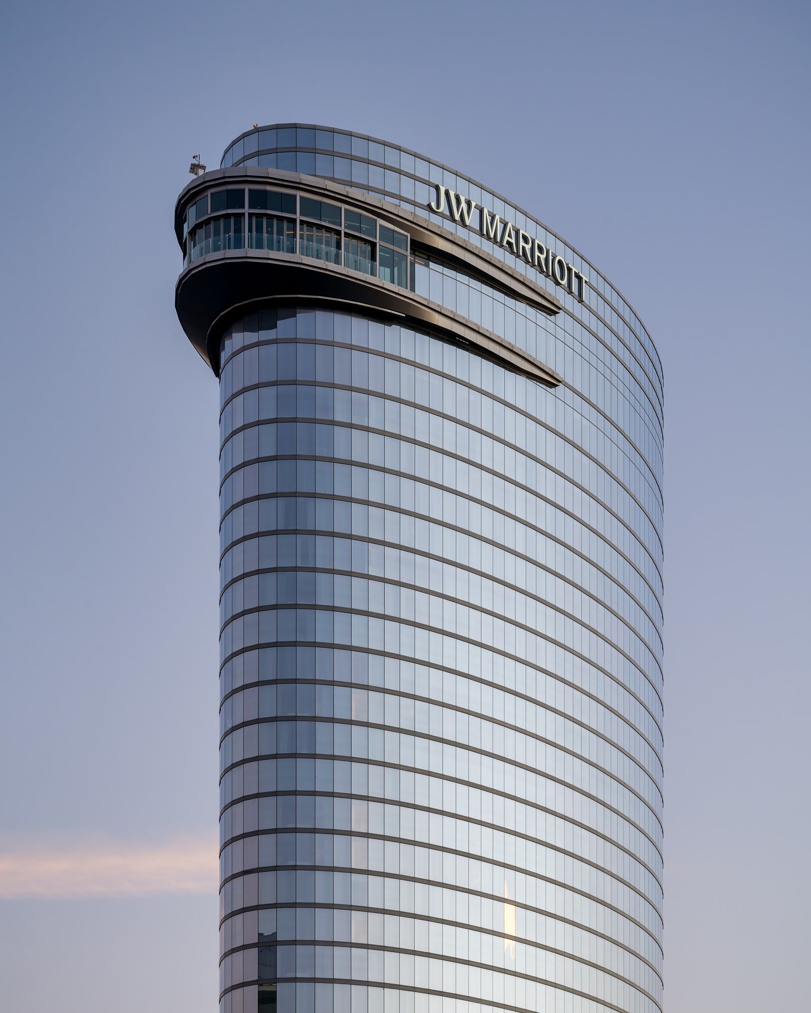 Curved JW Marriott tower exterior with reflective glass facade against a soft evening sky.