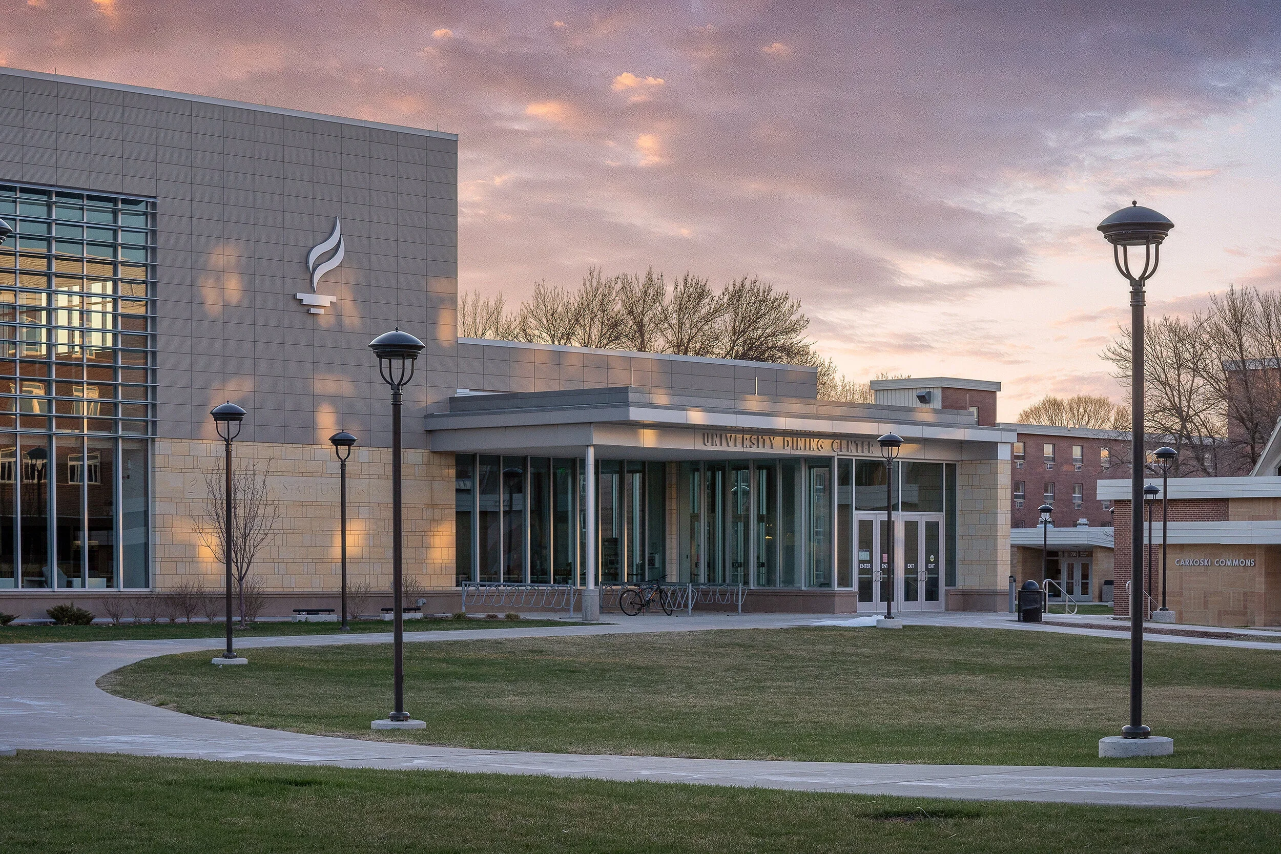 Contemporary academic building exterior with glass walls, metal panels, and a landscaped campus lawn.