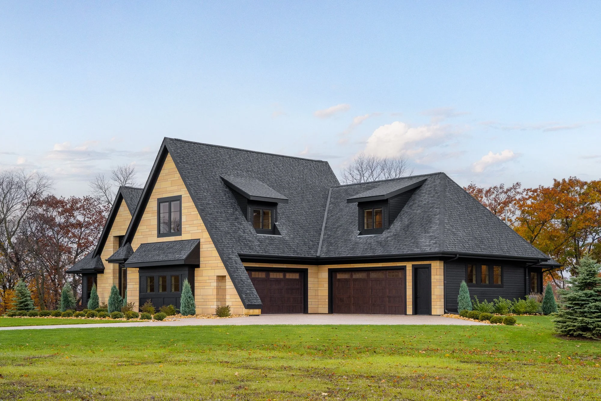 Angled view of a modern home with dark roofing, stone siding, and large windows.