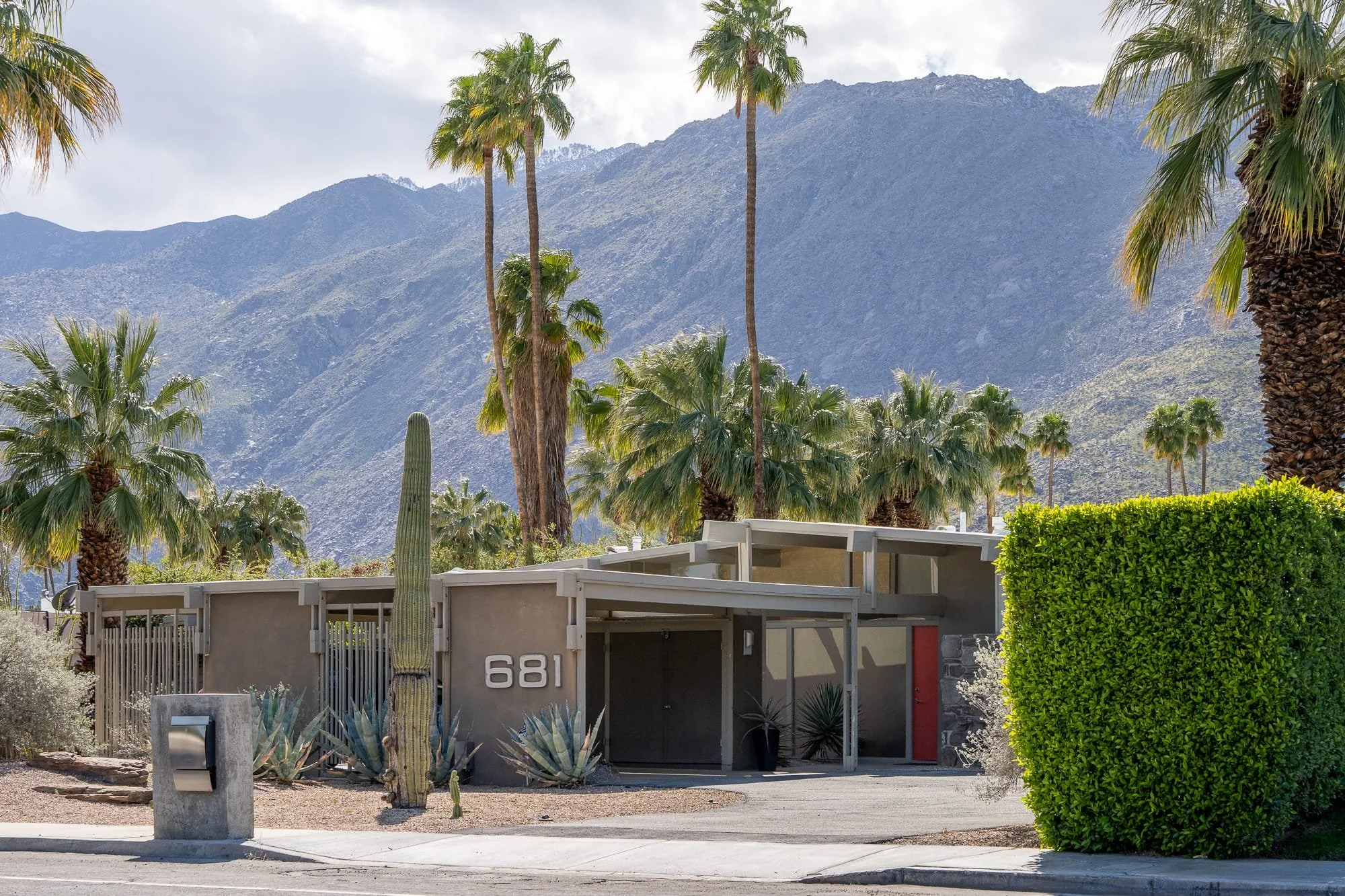 Desert modern home entry with stacked stone walls, metal rooflines, boulders, cactus, and drought-tolerant landscaping.