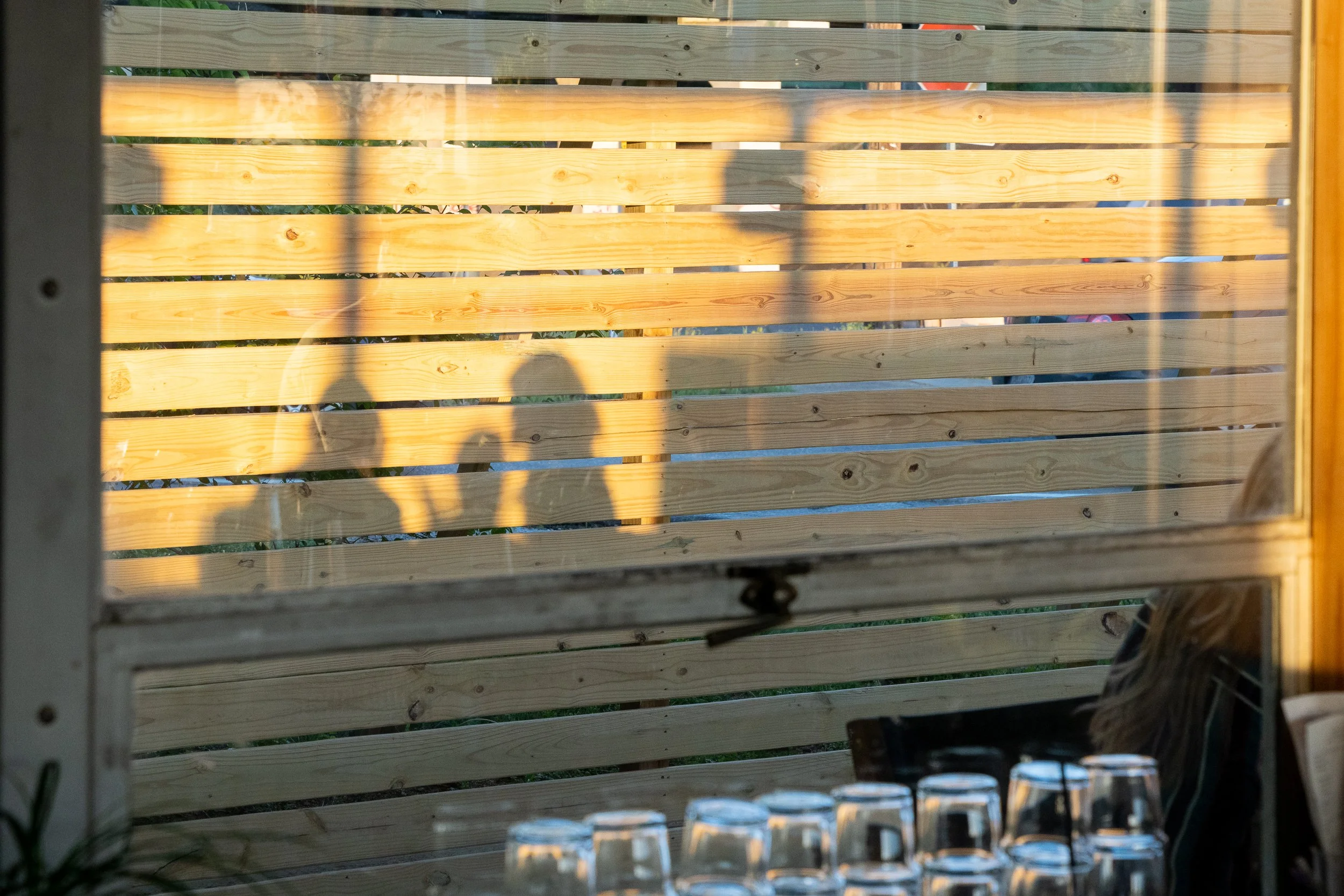 Shadows of guests cast onto a wooden slatted wall at sunset.