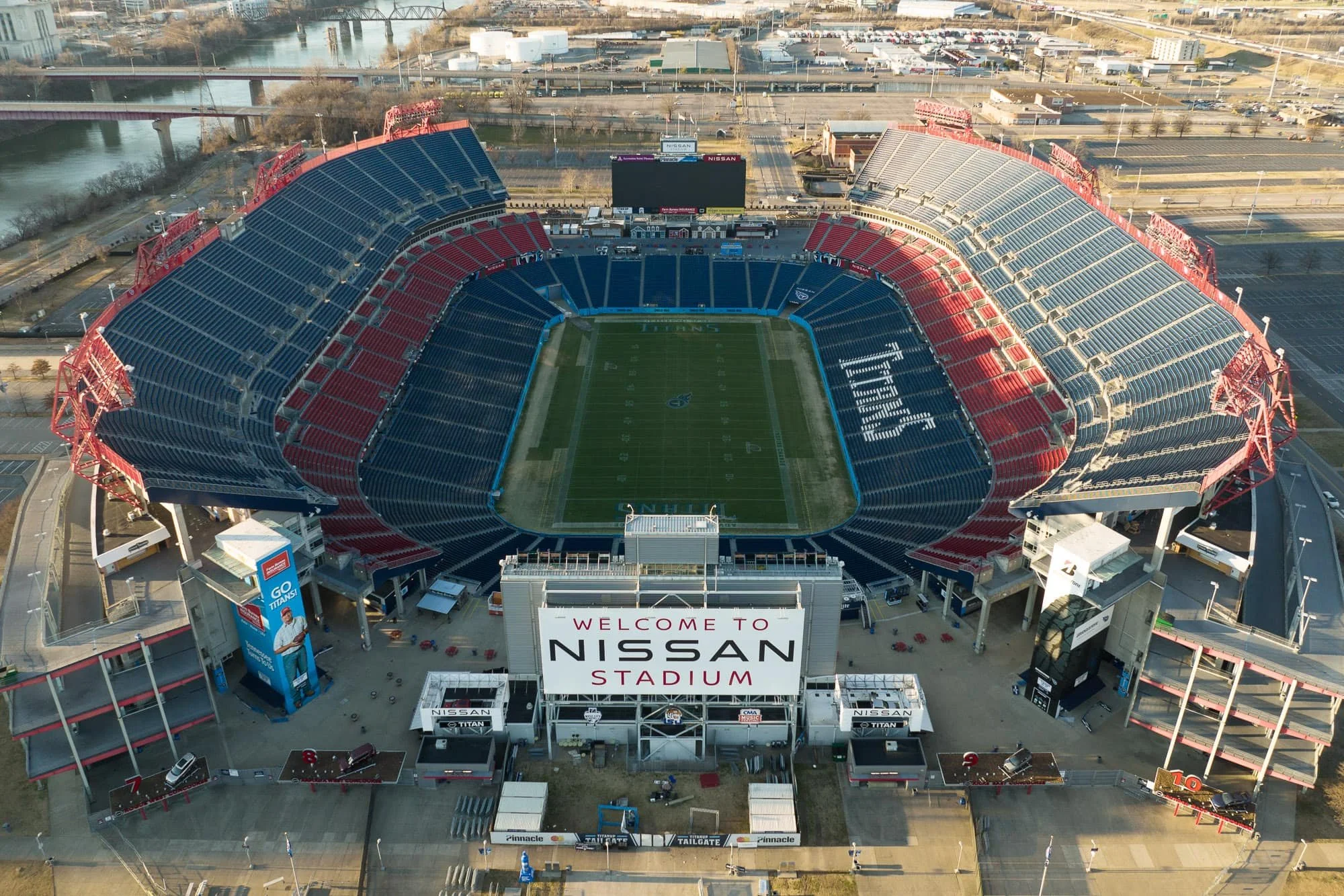 Straight down aerial view of Nissan Stadium Nashville showing the full oval footprint, green field, red and blue seating, and surrounding infrastructure