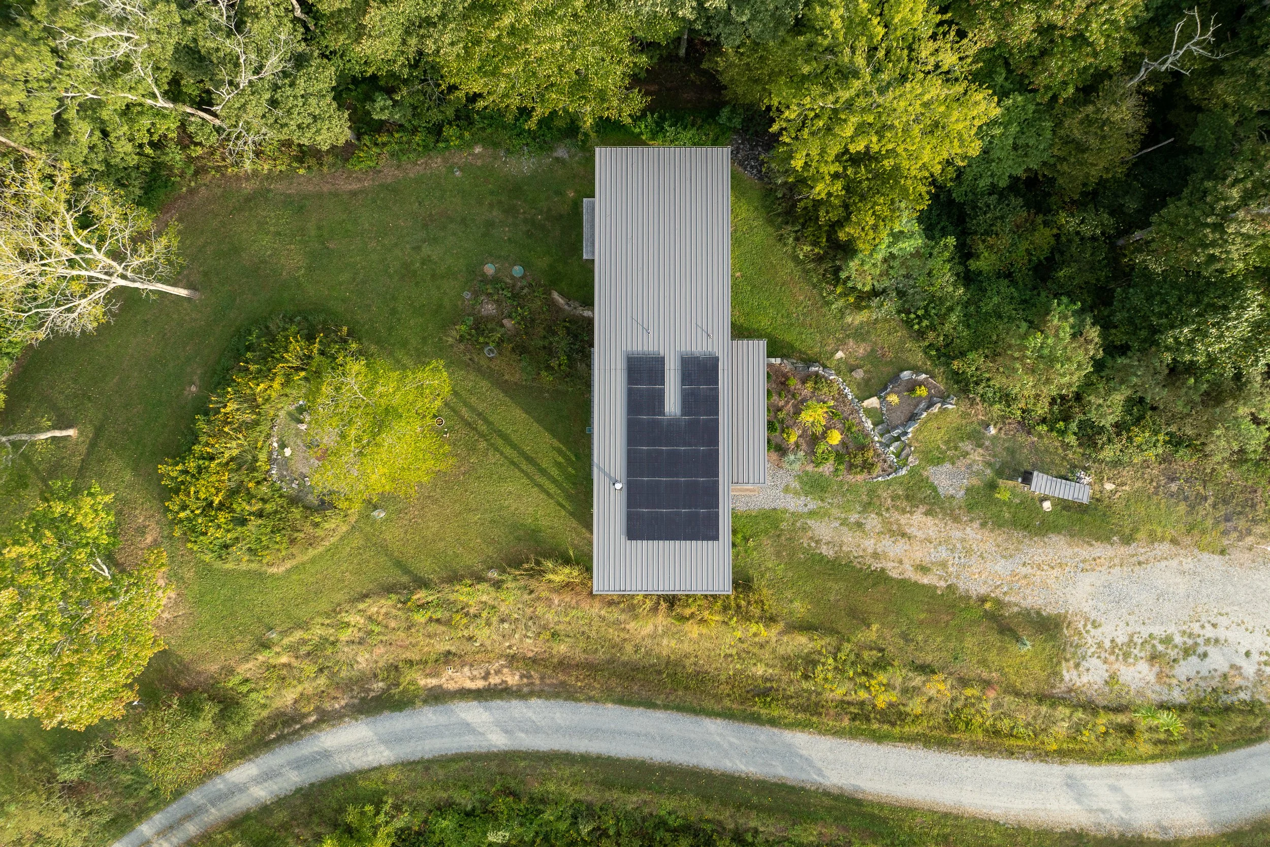 Aerial view of a modern home with solar panels surrounded by lush greenery.