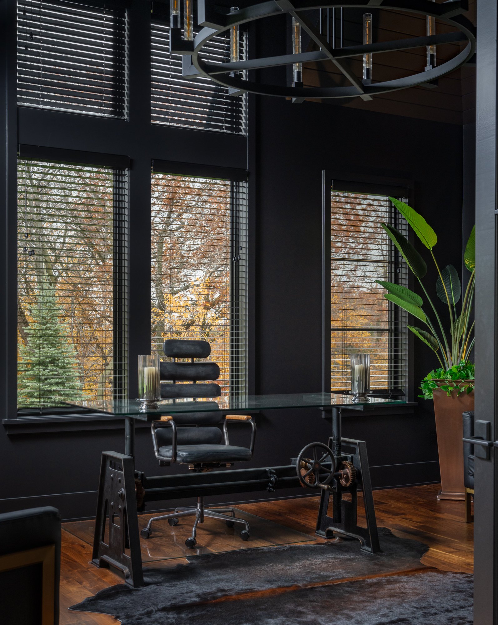 Luxury home office with dark walls, floor-to-ceiling windows, and a glass-top desk.