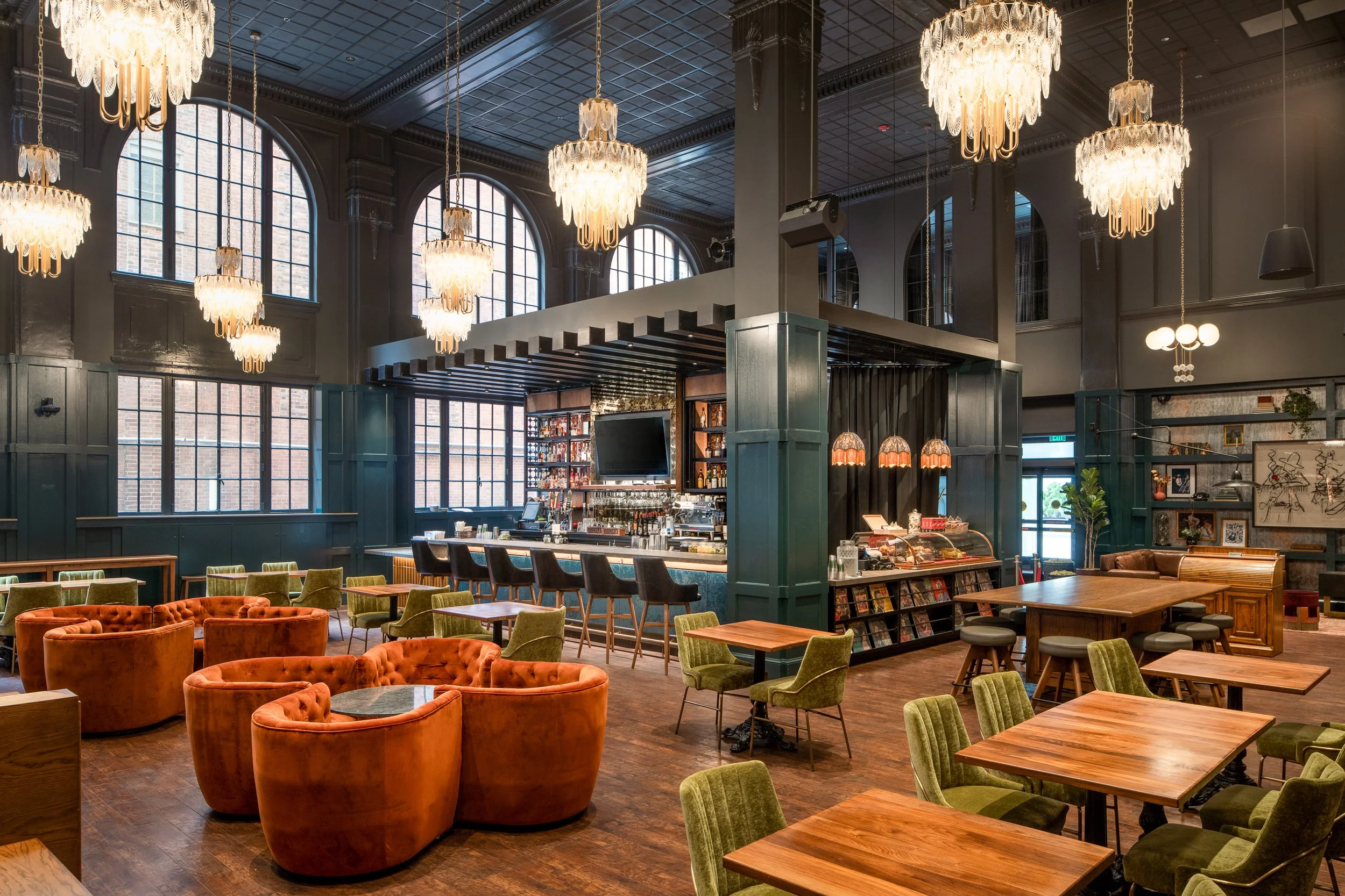 Grand lobby of a boutique hotel with dramatic chandeliers, dark walls, warm accent lighting, and layered seating areas