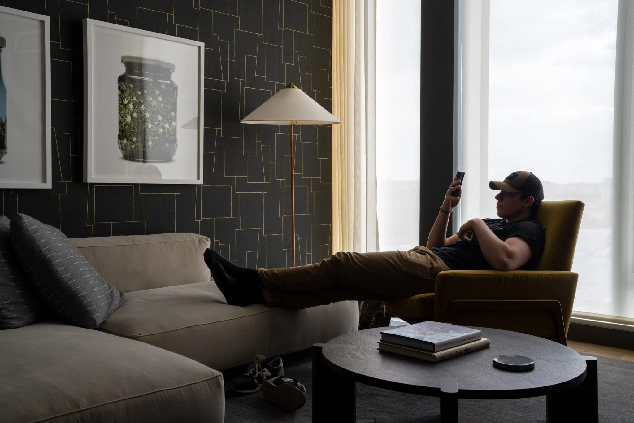Person relaxing in a modern living room beside a large window with patterned dark wallpaper.