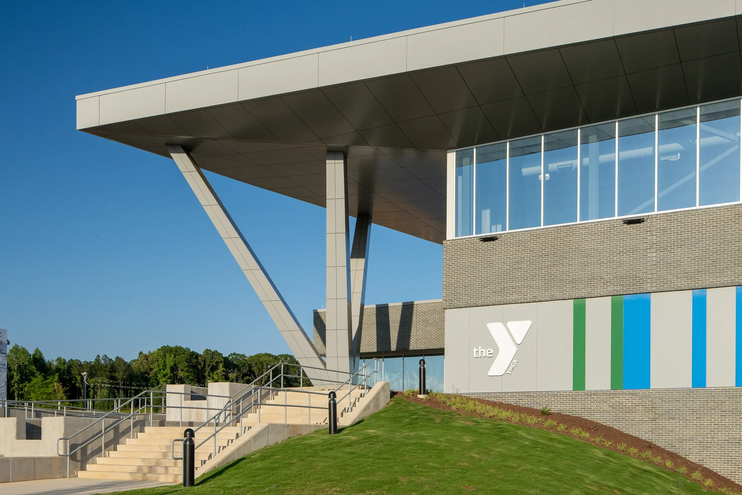 Landscaped entry approach with concrete stairs, YMCA signage, brick facade, glass walls and colorful panels.
