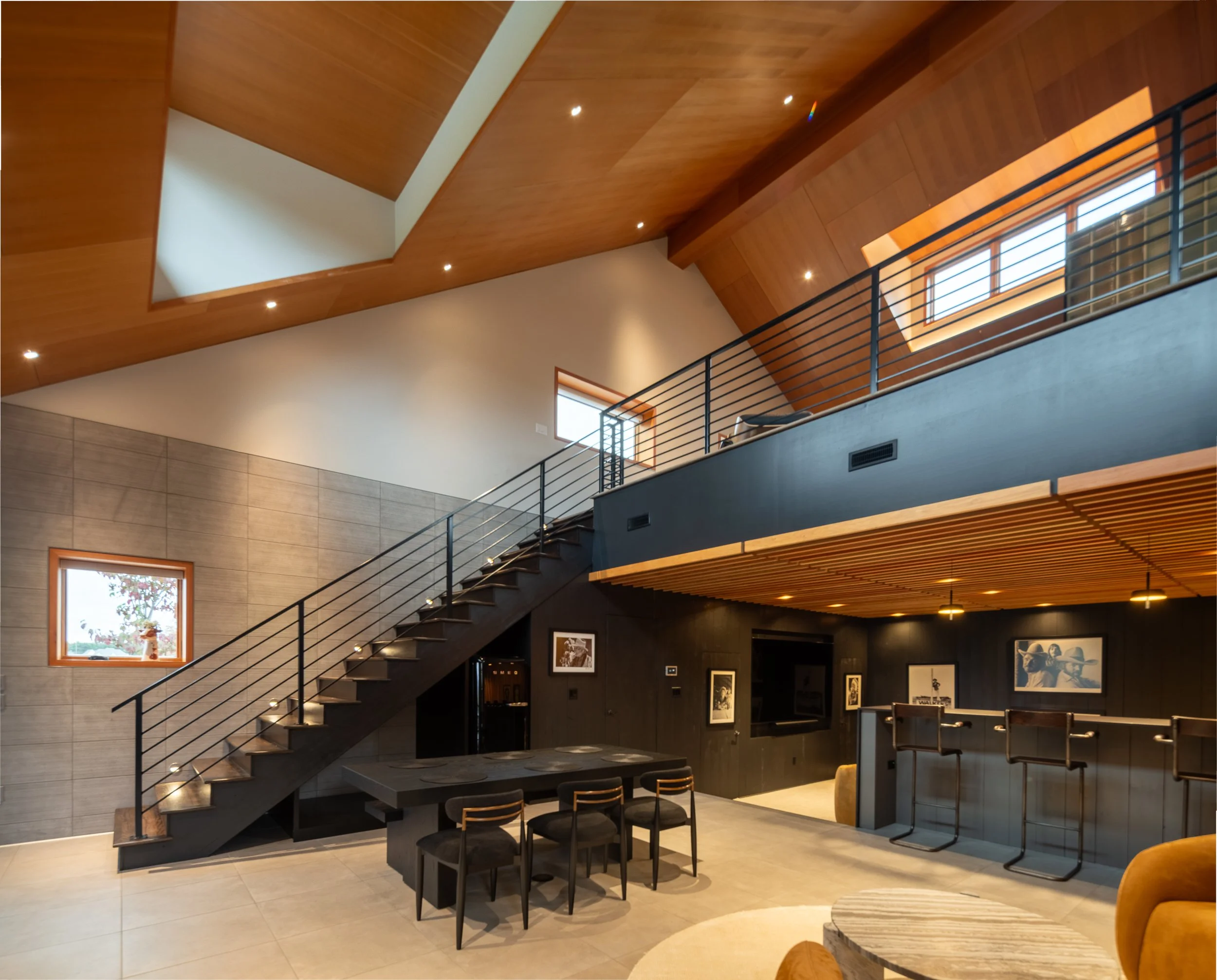 Open lounge with floating stair, black railing, high wood ceiling, and dark built-ins.