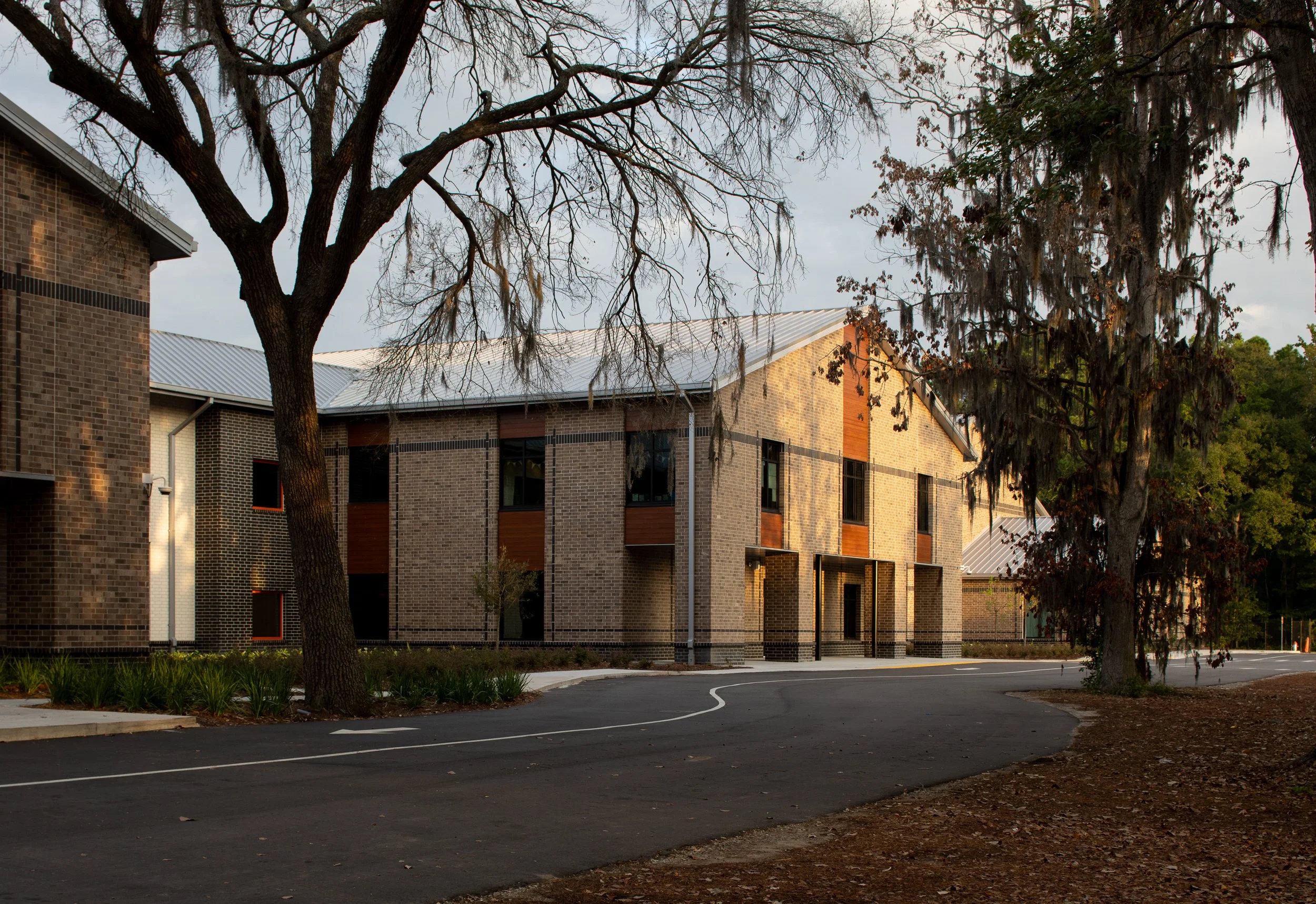 Brick school building in Beaufort, SC framed by live oaks and Spanish moss, with morning light across the facade and entry drive.