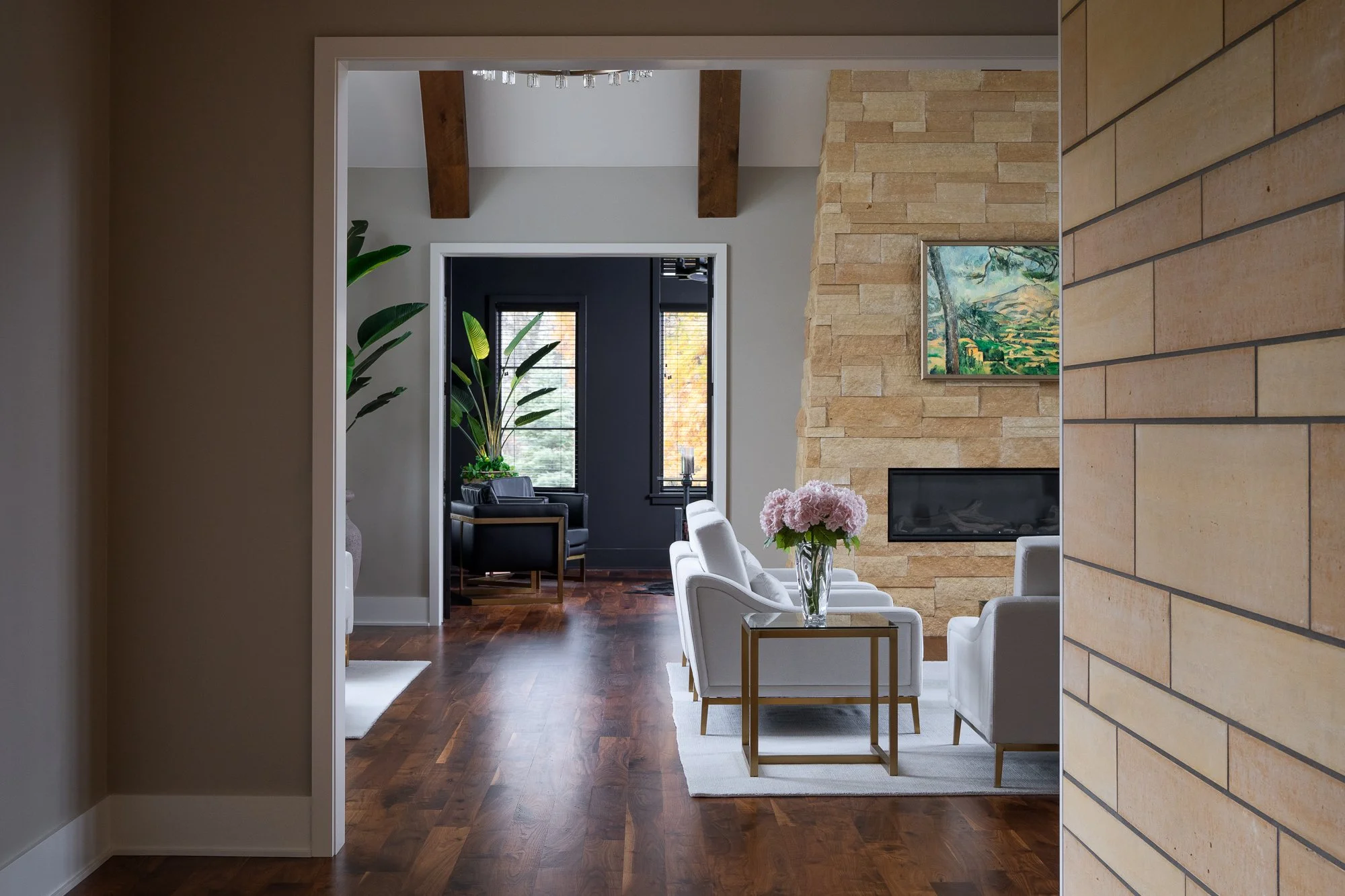 Open-concept living room featuring a stone fireplace, wooden beams, and elegant furnishings.