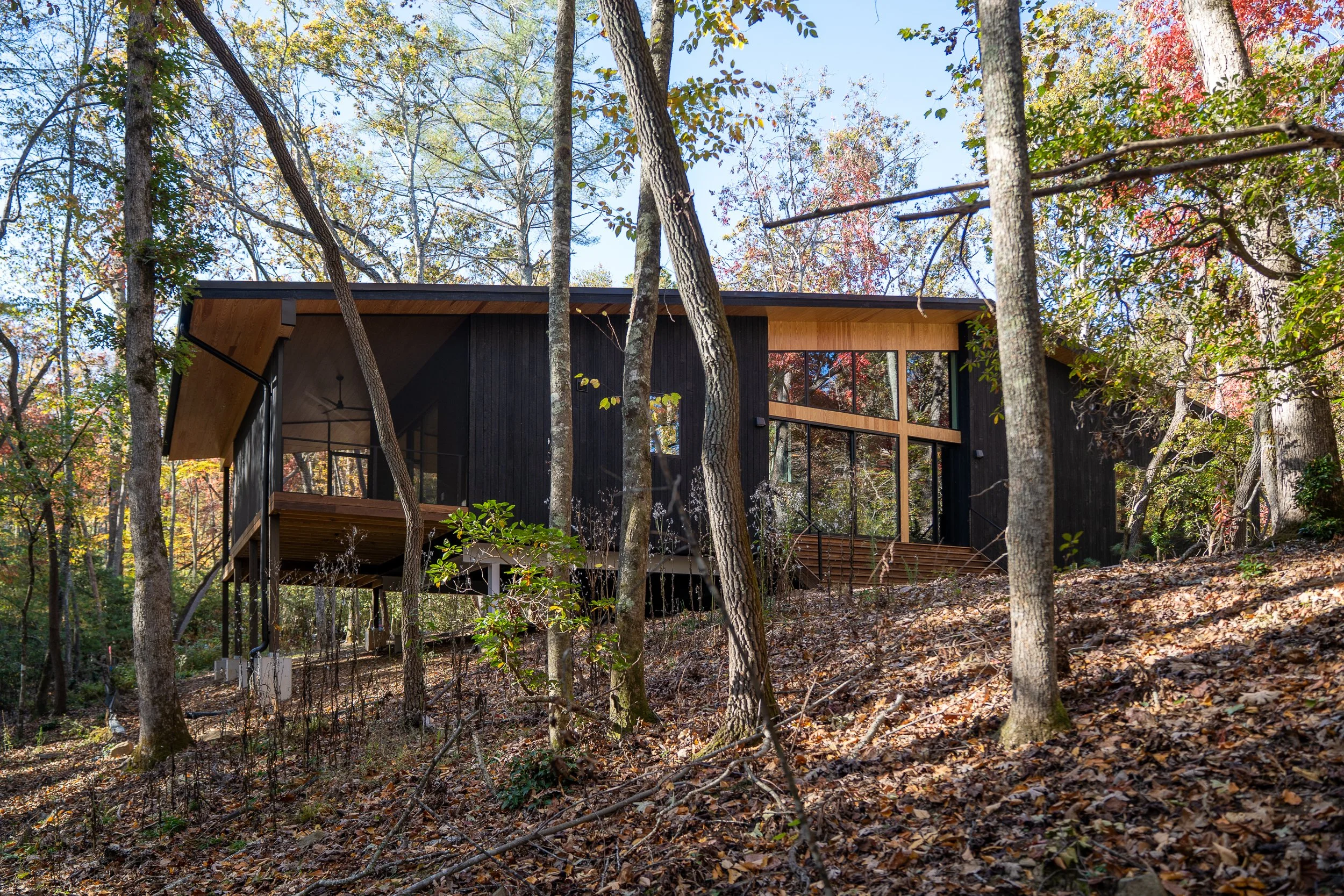 Hillside view of the home with burnt cedar siding, tall windows, and structure lifted above the ground.