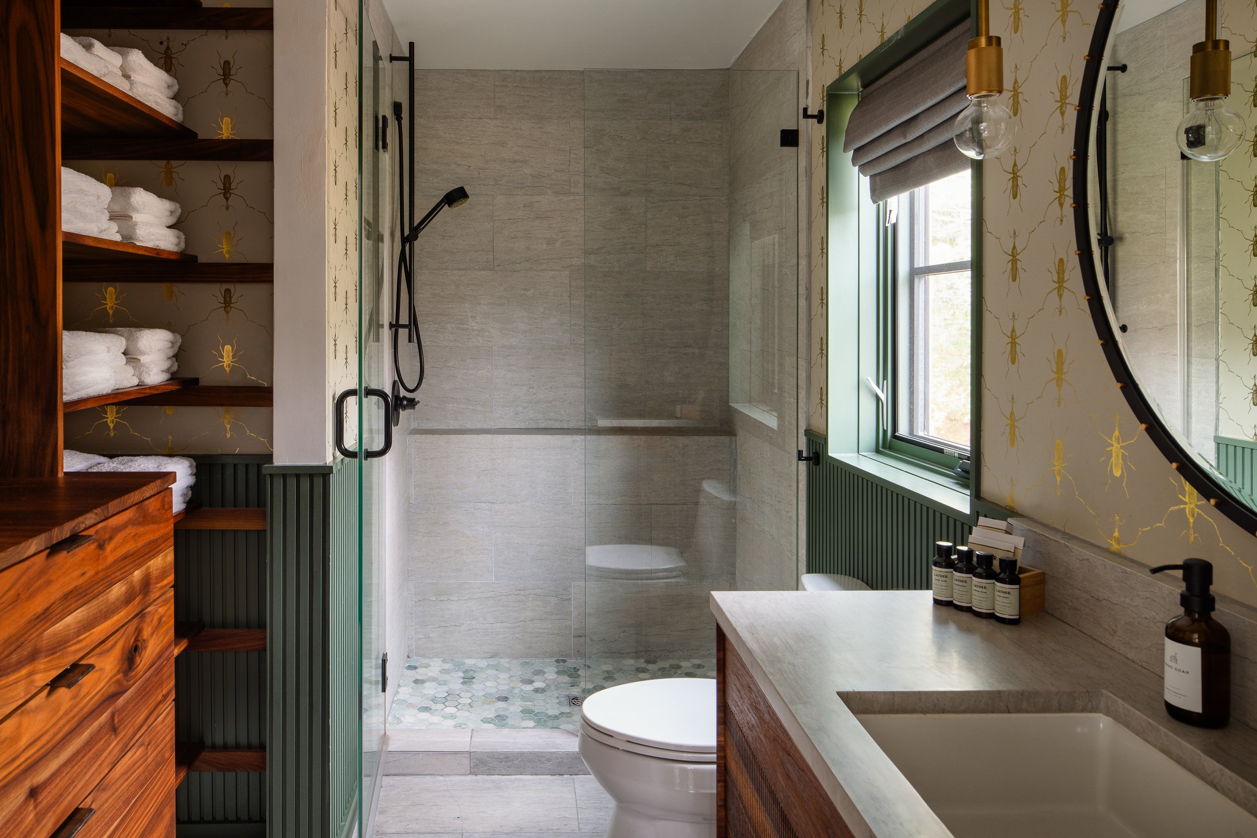 Bathroom with green trim, insect-pattern wallpaper, wood vanity, open towel shelving, and glass shower.