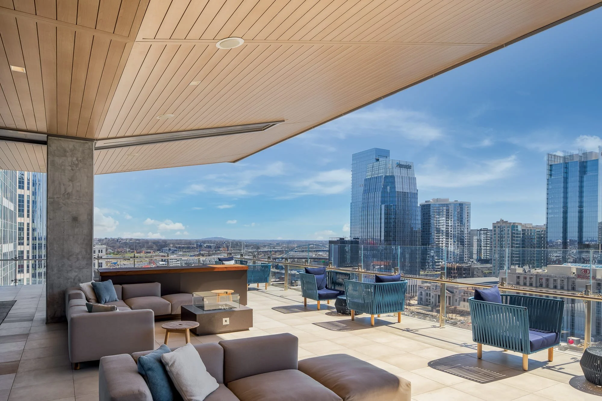 Rooftop terrace at Alliance Bernstein Nashville with outdoor lounge seating, a fire feature, wood slat ceiling, glass railings, and panoramic views of the downtown skyline