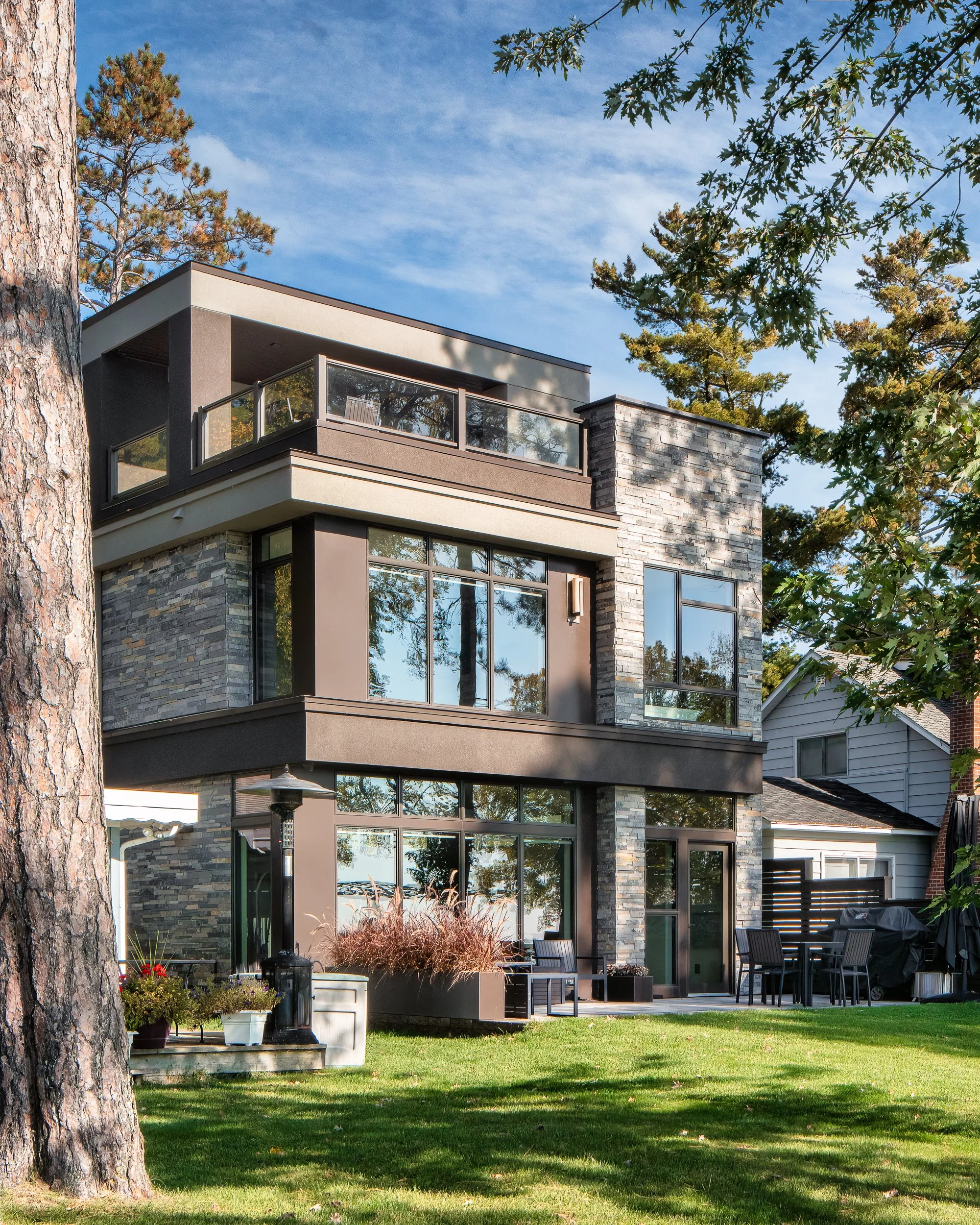 Rear view of a modern home with stone accents, large windows, and a lakefront setting.