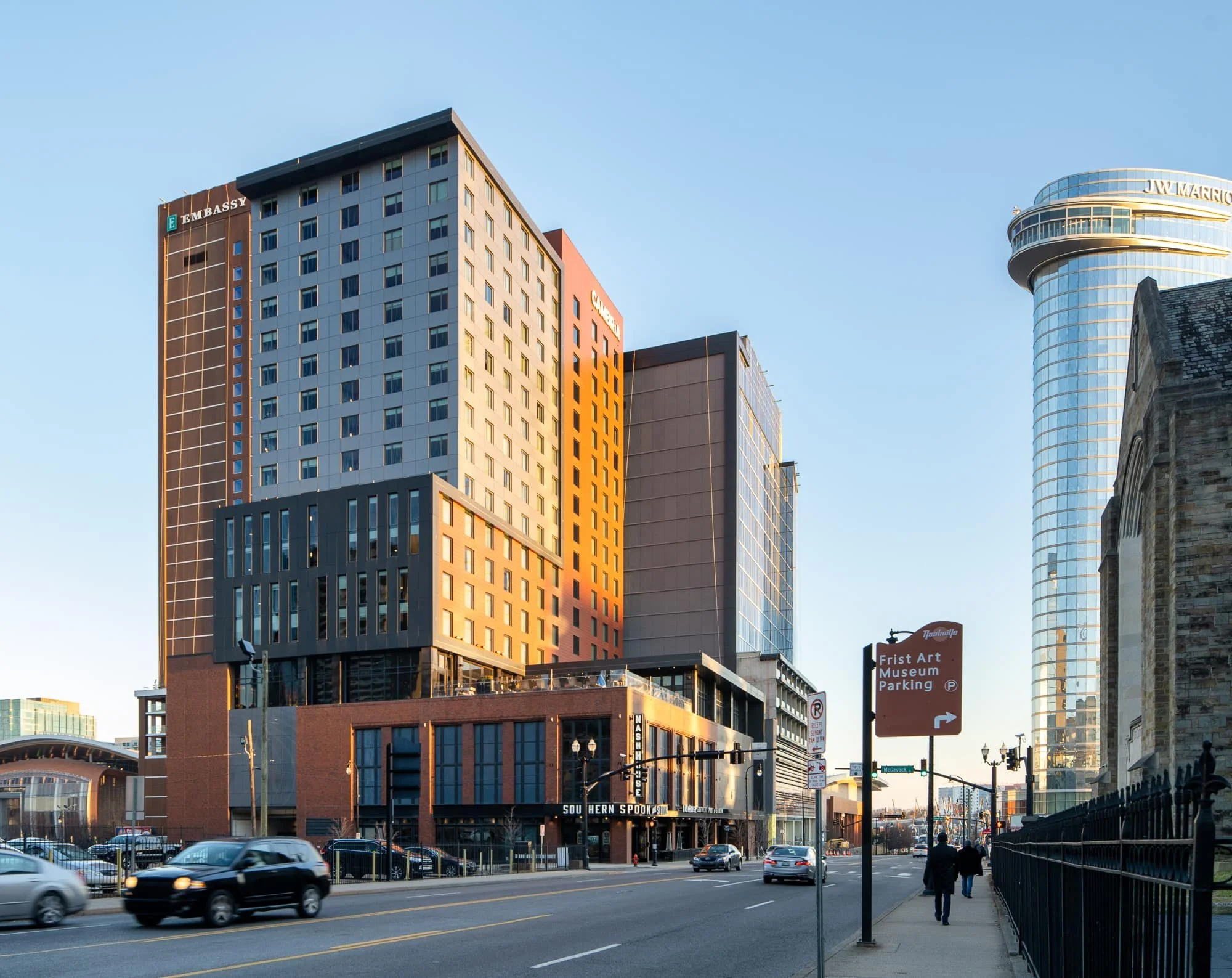 Cambria Hotel and adjacent JW Marriott in downtown Nashville at street level with the embassy building to the left and ground floor signage including NashHouse Southern Spoon and Saloon visible